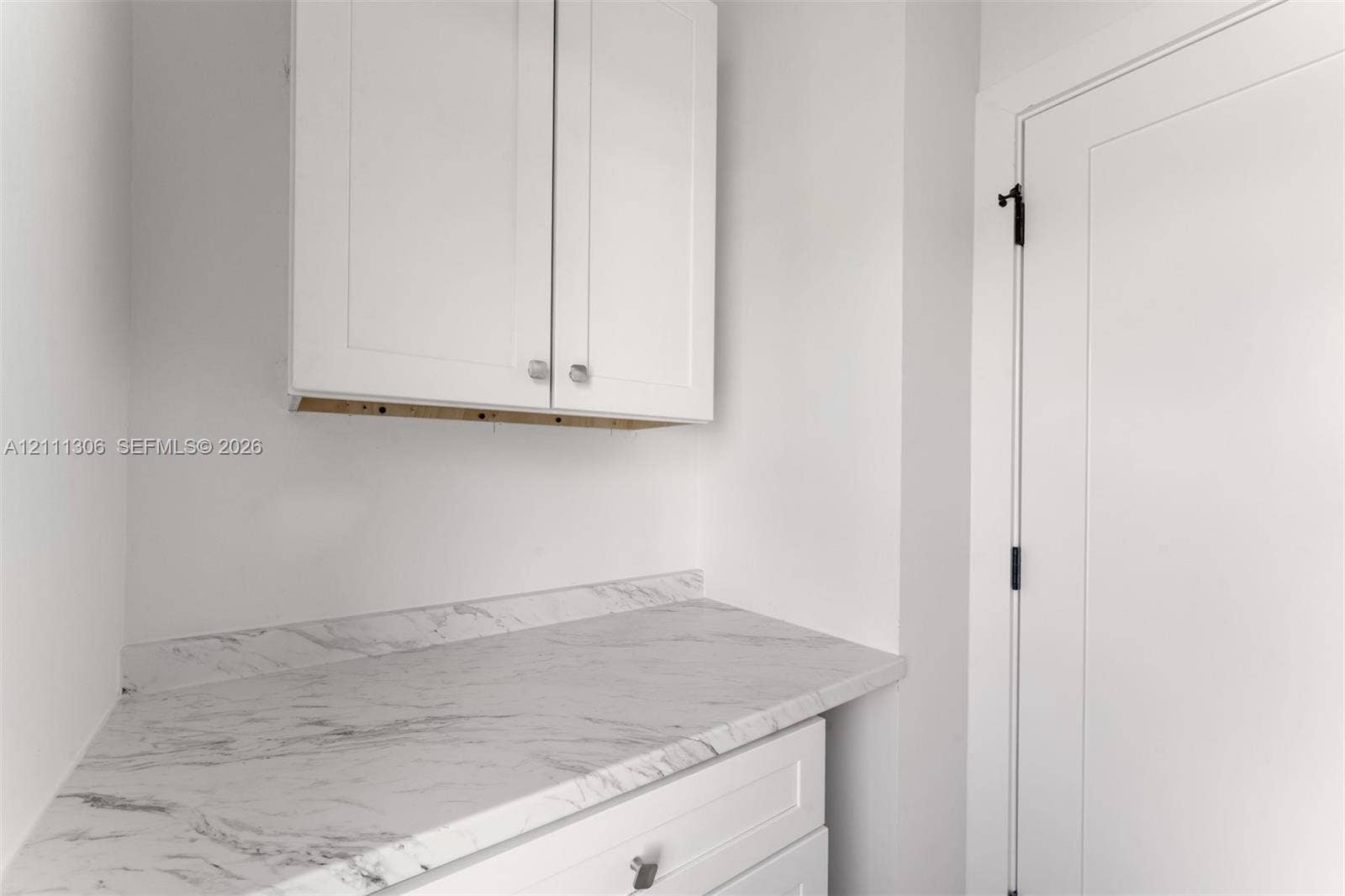 Shaker-style white cabinetry, stone-finish countertop with matching backsplash, and solid-core door with matte black hardware