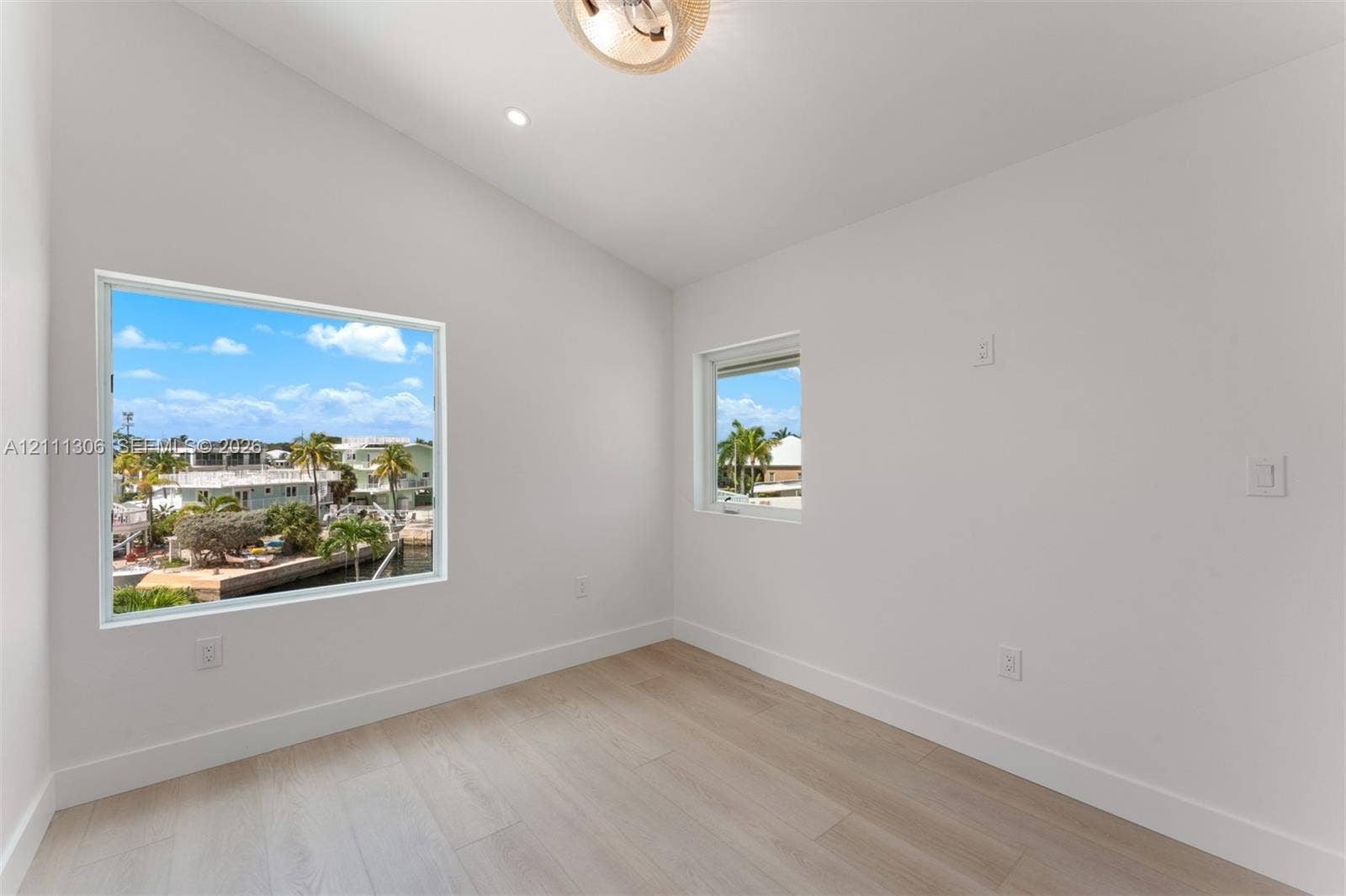 Bright room featuring a vaulted ceiling, wood-finish flooring, recessed lighting, and large windows with water and palm tree scenery