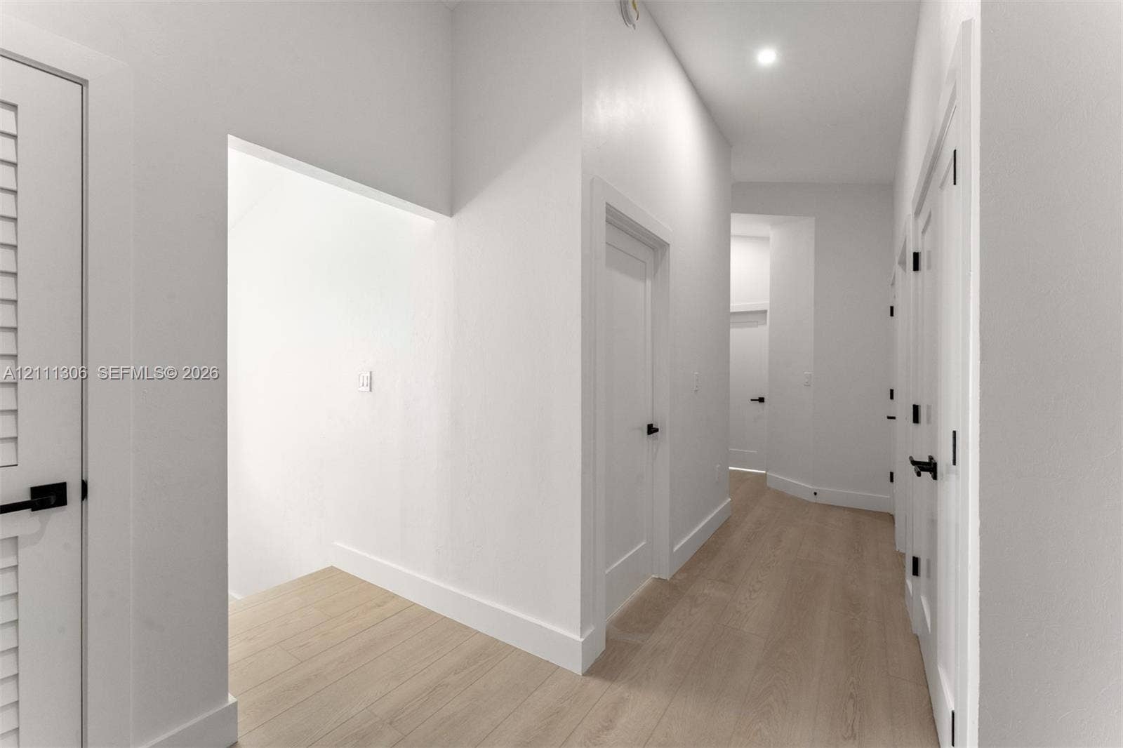 Hallway featuring wood-finish flooring, shaker-style interior doors, matte black hardware, and recessed lighting