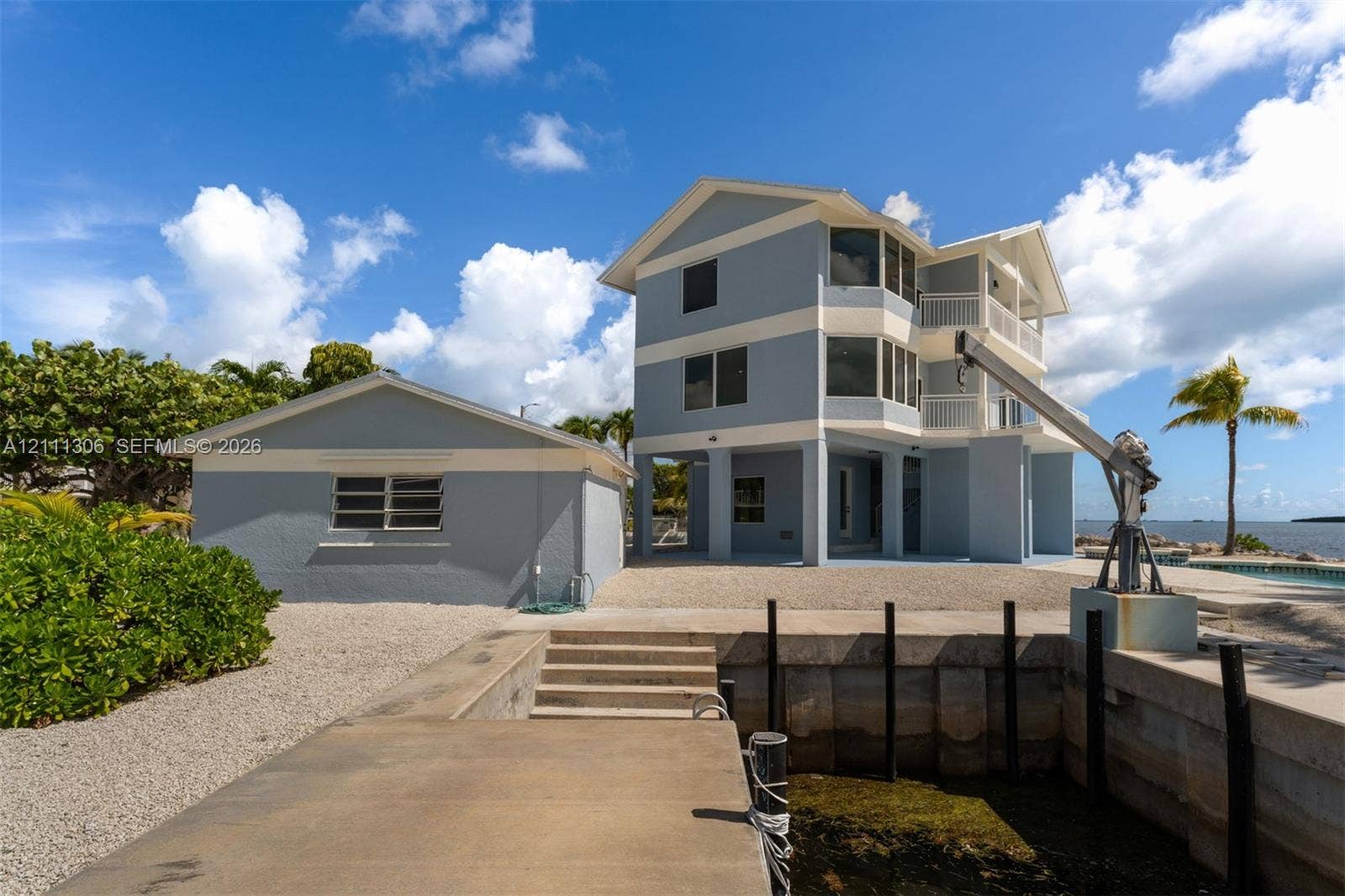 Multi-story residence featuring elevated balconies, a detached structure, a private concrete boat dock with a mechanical lift, and concrete seawall