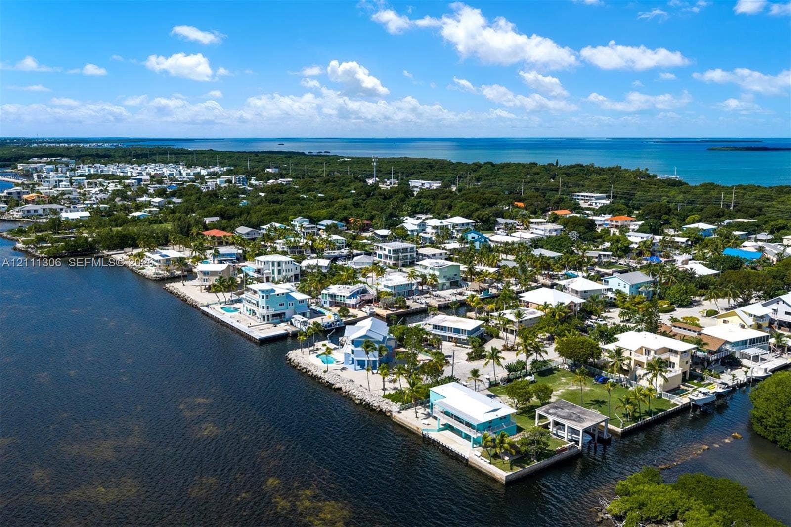 Aerial perspective of a coastal property featuring direct waterfront access, a private boat dock, a sea wall, and expansive open-water scenery