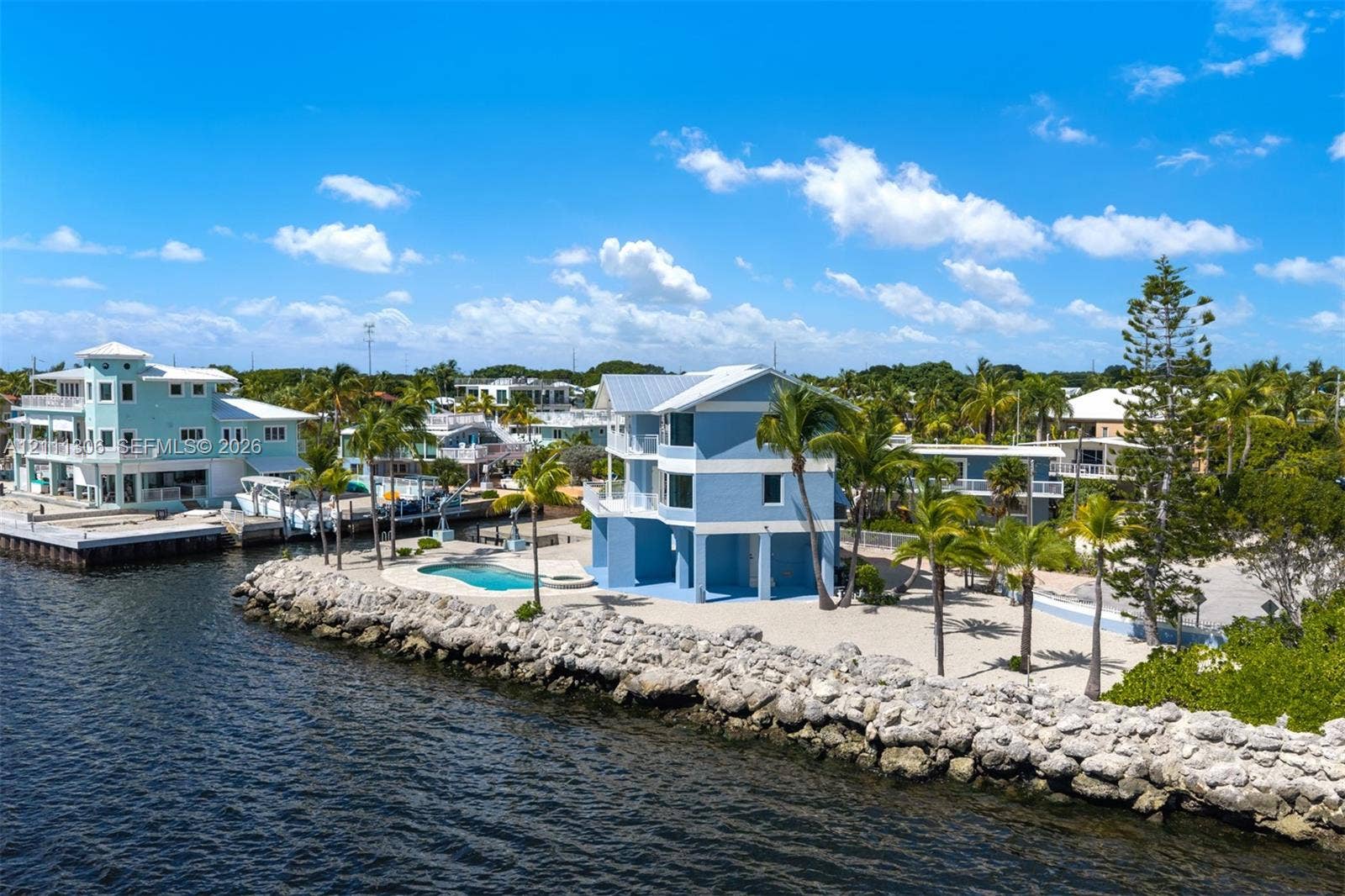 Waterfront residence featuring a metal roof, multi-level balconies, an in-ground swimming pool, and stone-reinforced shoreline