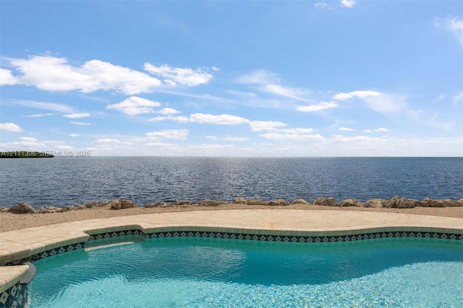 Inground swimming pool with tiled coping, stone-paver pool deck, and natural rock shoreline