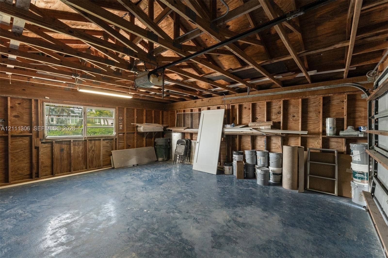 Garage featuring exposed wood framing, painted concrete flooring, an integrated automatic garage door opener, and a single-pane horizontal window