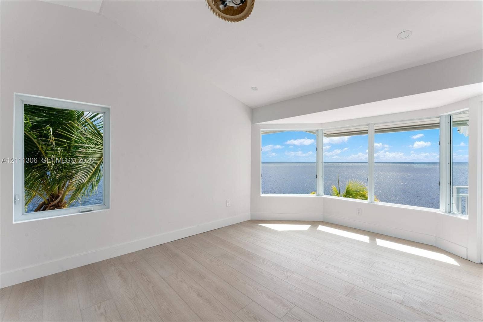 Vaulted ceiling, wood-finish flooring, bay window, and water backdrop