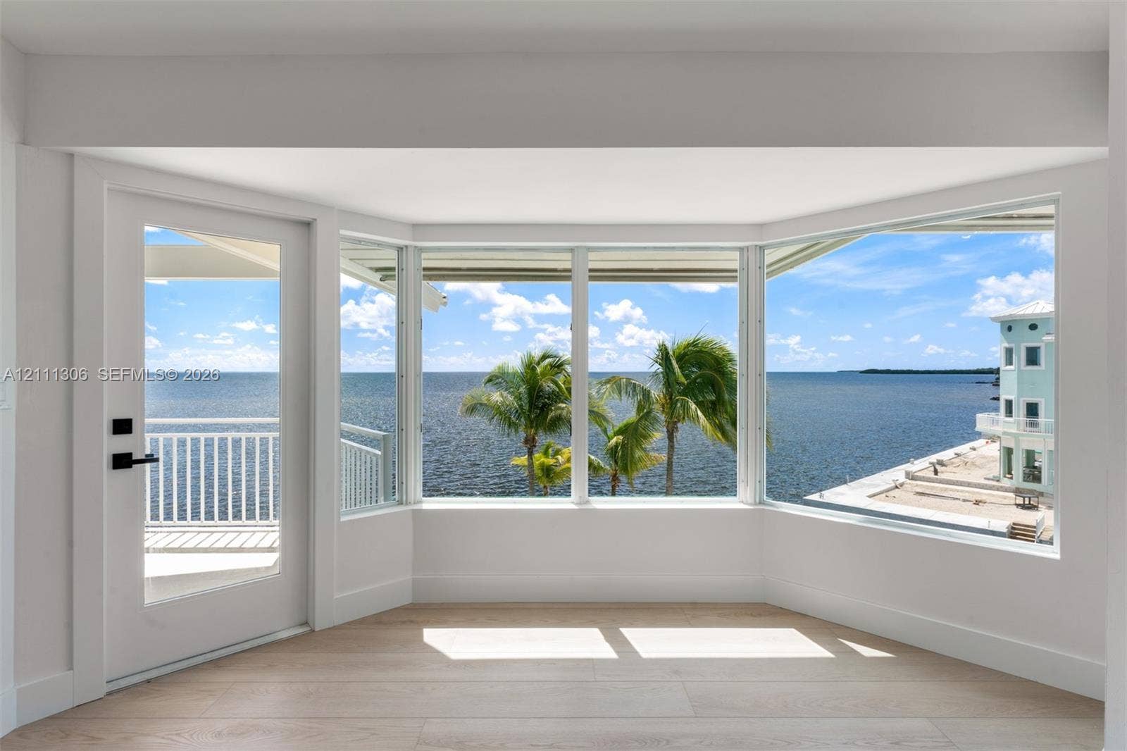 Bay window with expansive water-facing glass, light-toned wood-finish flooring, and glass-paned exterior door with hardware