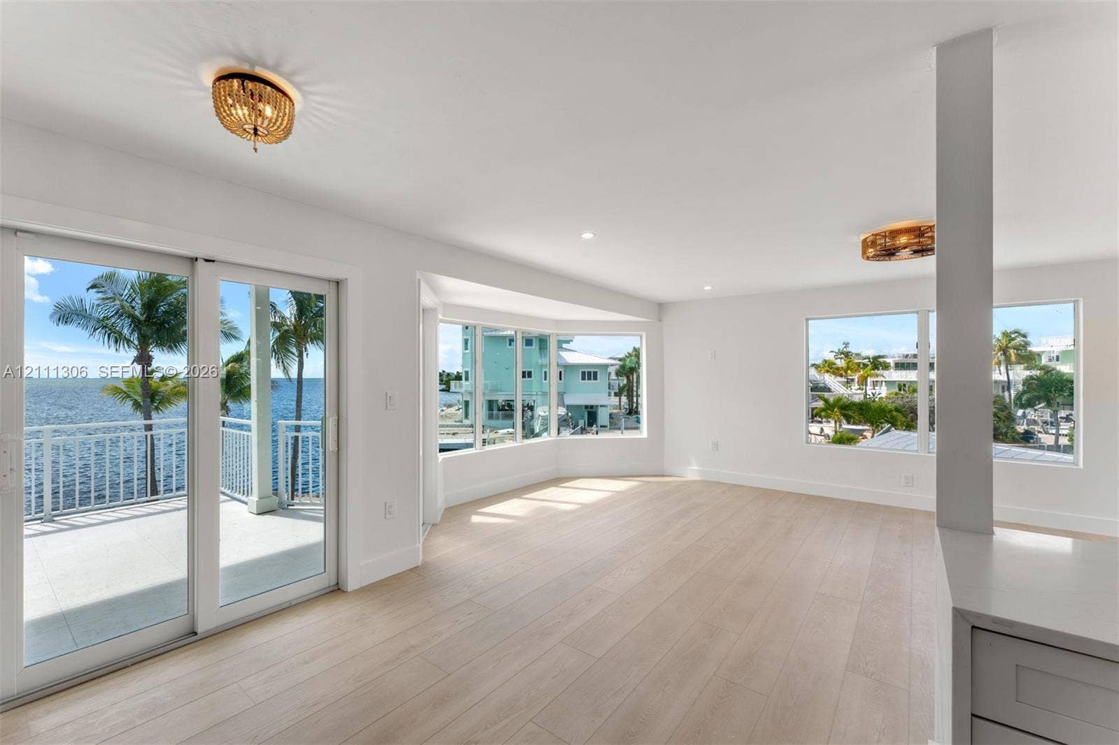 Light-filled interior featuring expansive wood-finish flooring, a bay window, sliding glass doors to a balcony, and decorative circular flush-mount lighting fixtures