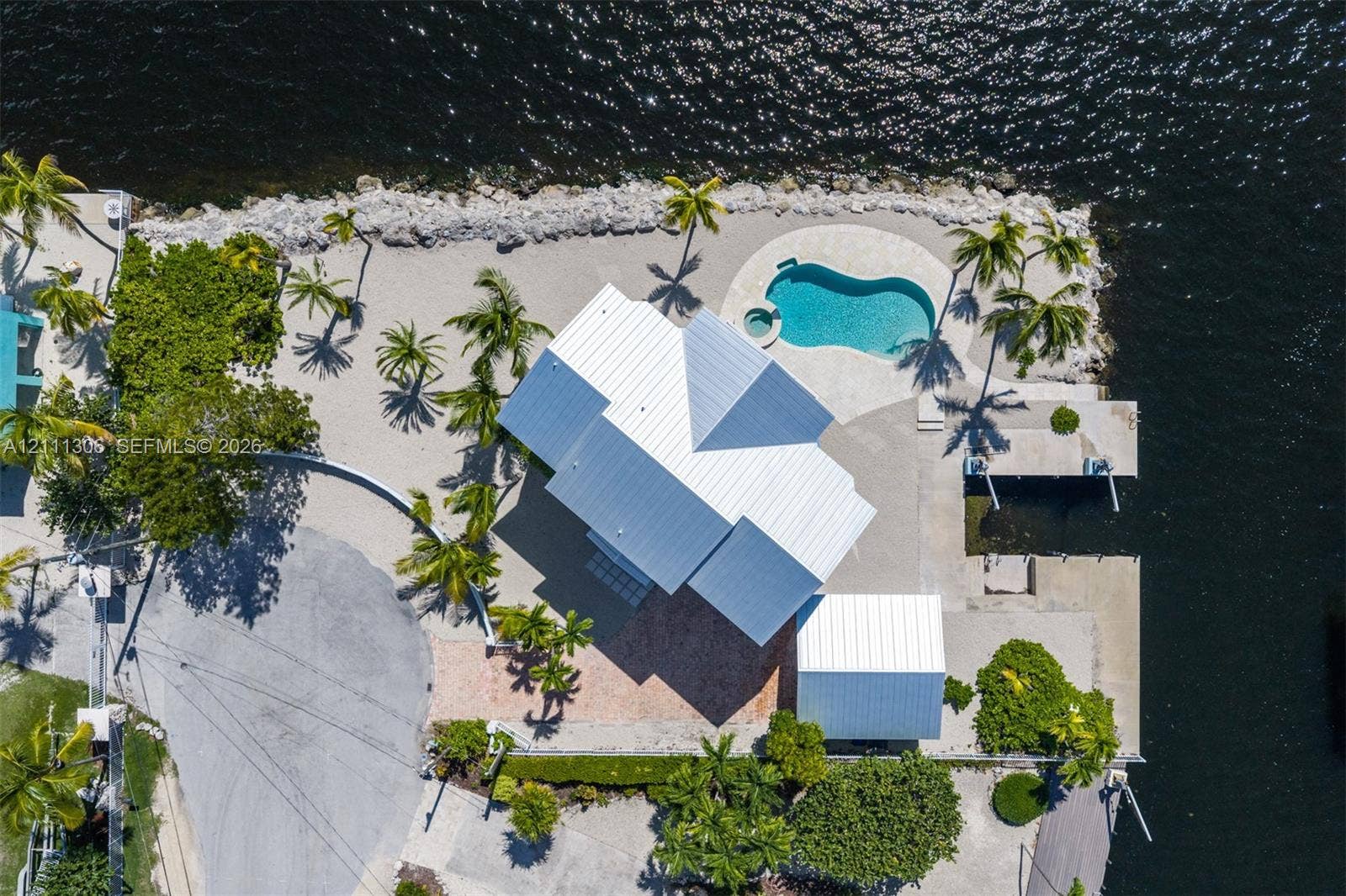 Waterfront property featuring a metal roof, private dock, in-ground swimming pool with spa, and paved hardscaping