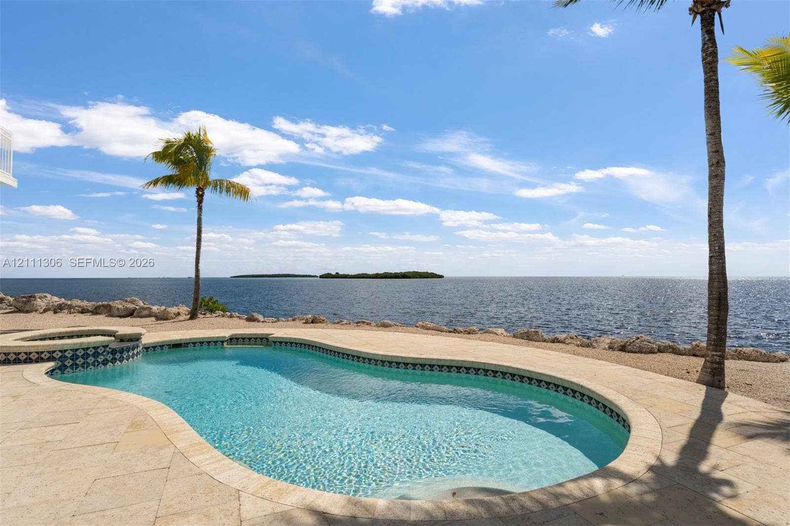 Custom-shaped swimming pool with decorative tile border, integrated spa, and natural stone pool deck bordering an open water shoreline