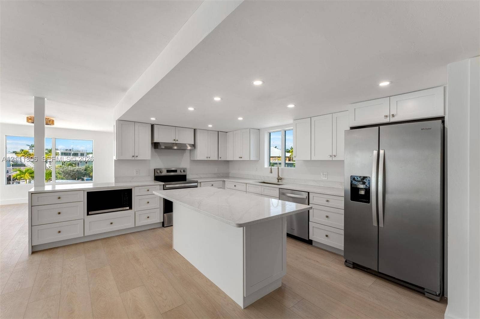 Kitchen featuring white shaker-style cabinetry, quartz countertops, a central island, wood-finish flooring, and stainless steel appliances
