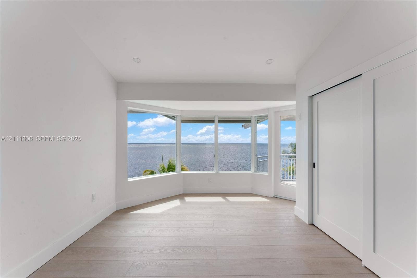 Bay window with expansive water scenery, recessed lighting, wood-finish flooring, and sliding door access to a balcony