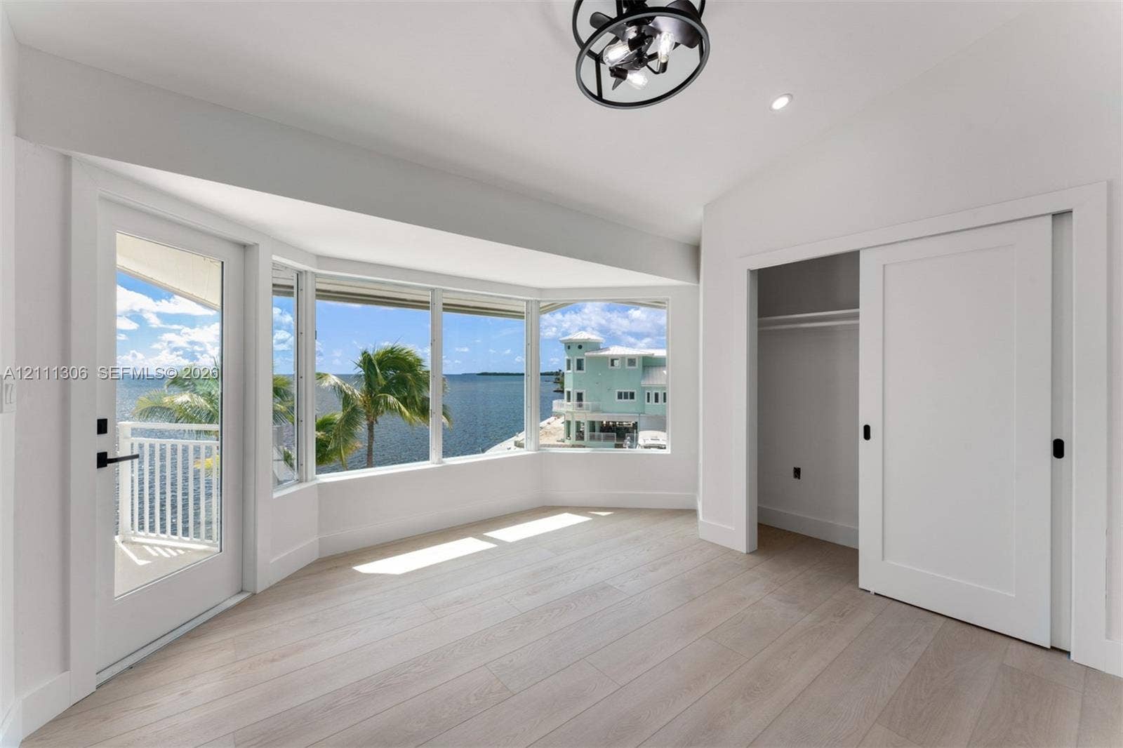 Bay window featuring expansive water scenery, wood-finish flooring, sliding door access to a private balcony, and a modern industrial-style ceiling fixture