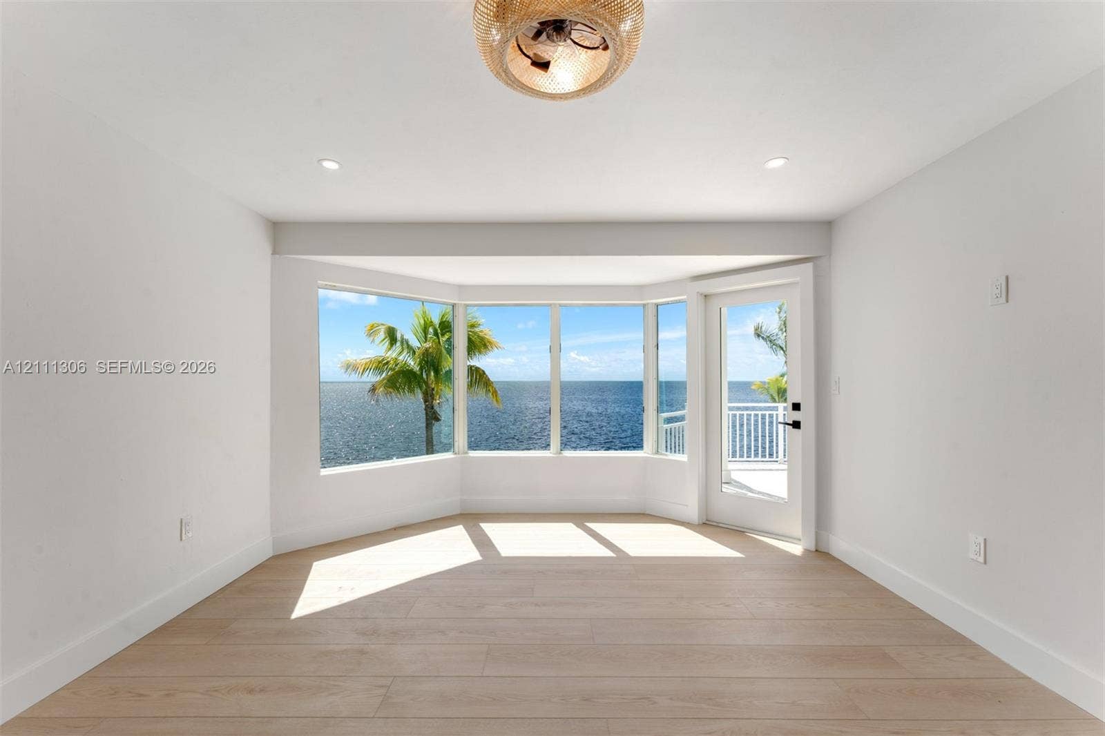 Bay window with water backdrop, wood-finish flooring, recessed lighting, woven-texture ceiling fixture, and glass-paneled exterior door