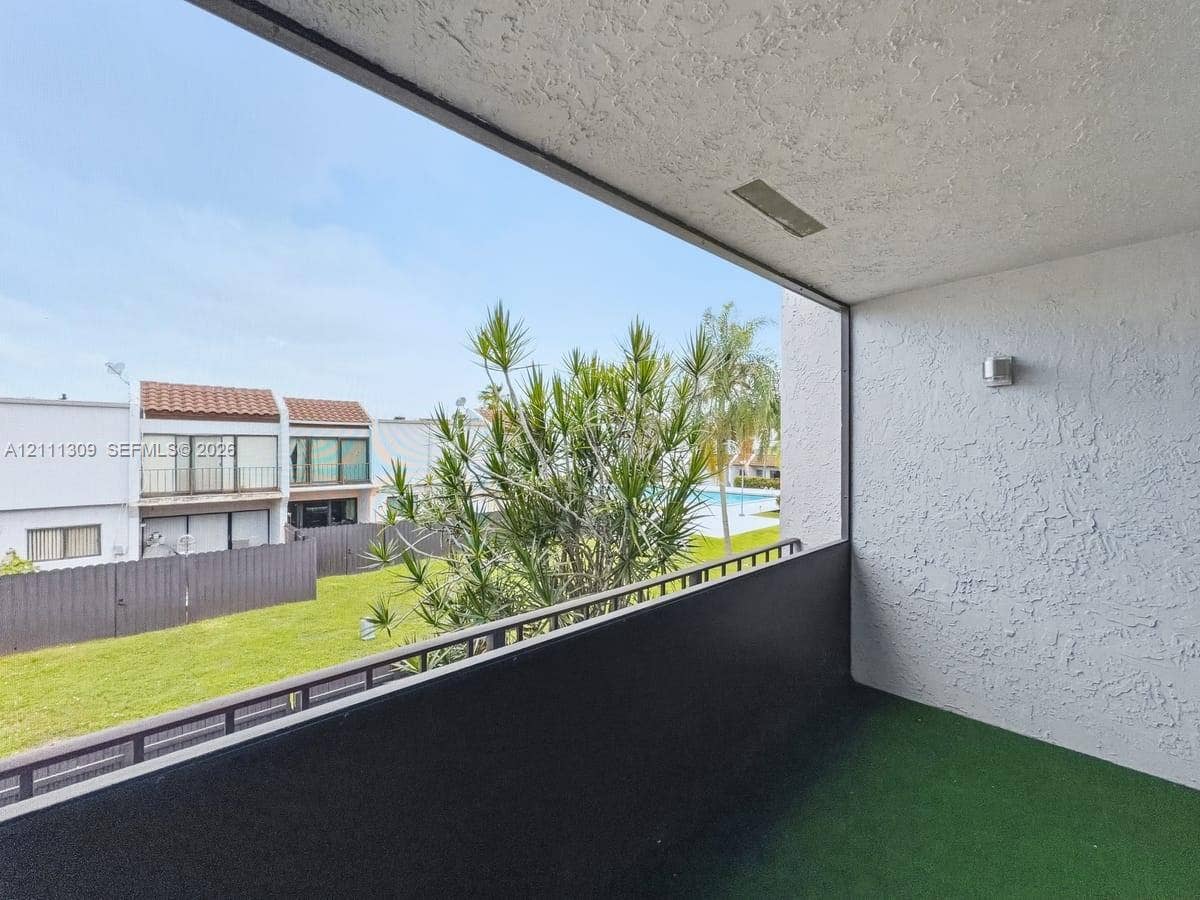 6518 Kendale Lakes Drive, #809, Miami, Miami, FL 33183 Covered balcony featuring textured stucco walls, a dark metal railing, and an exterior wall-mounted light fixture