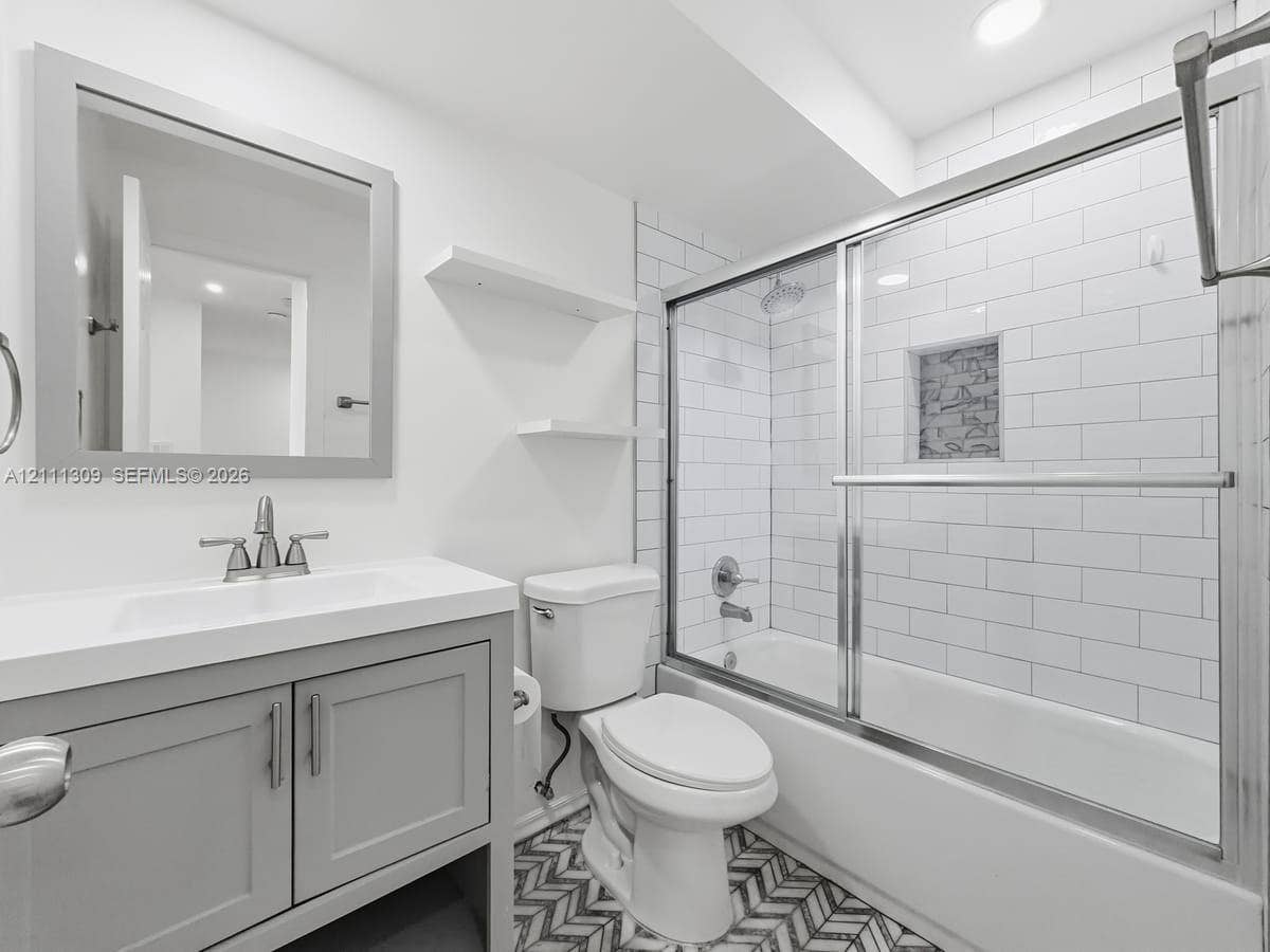 6518 Kendale Lakes Drive, #809, Miami, Miami, FL 33183 Grey vanity cabinet with integrated sink and countertop, white subway tile shower surround with built-in wall niche, glass sliding shower door, and patterned tile flooring