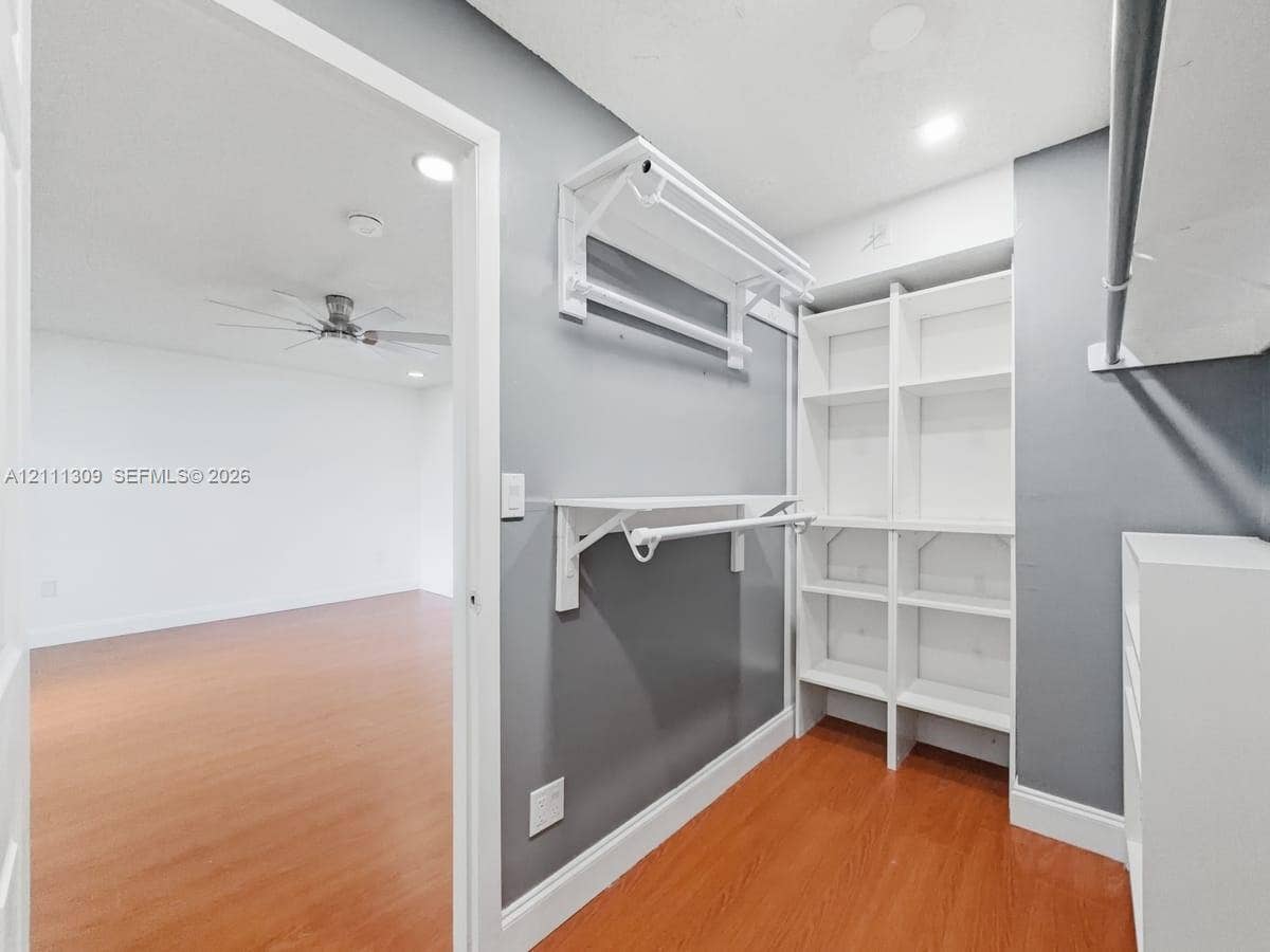 6518 Kendale Lakes Drive, #809, Miami, Miami, FL 33183 Walk-in closet featuring white built-in shelving, dual-tier hanging rods, and wood-finish flooring