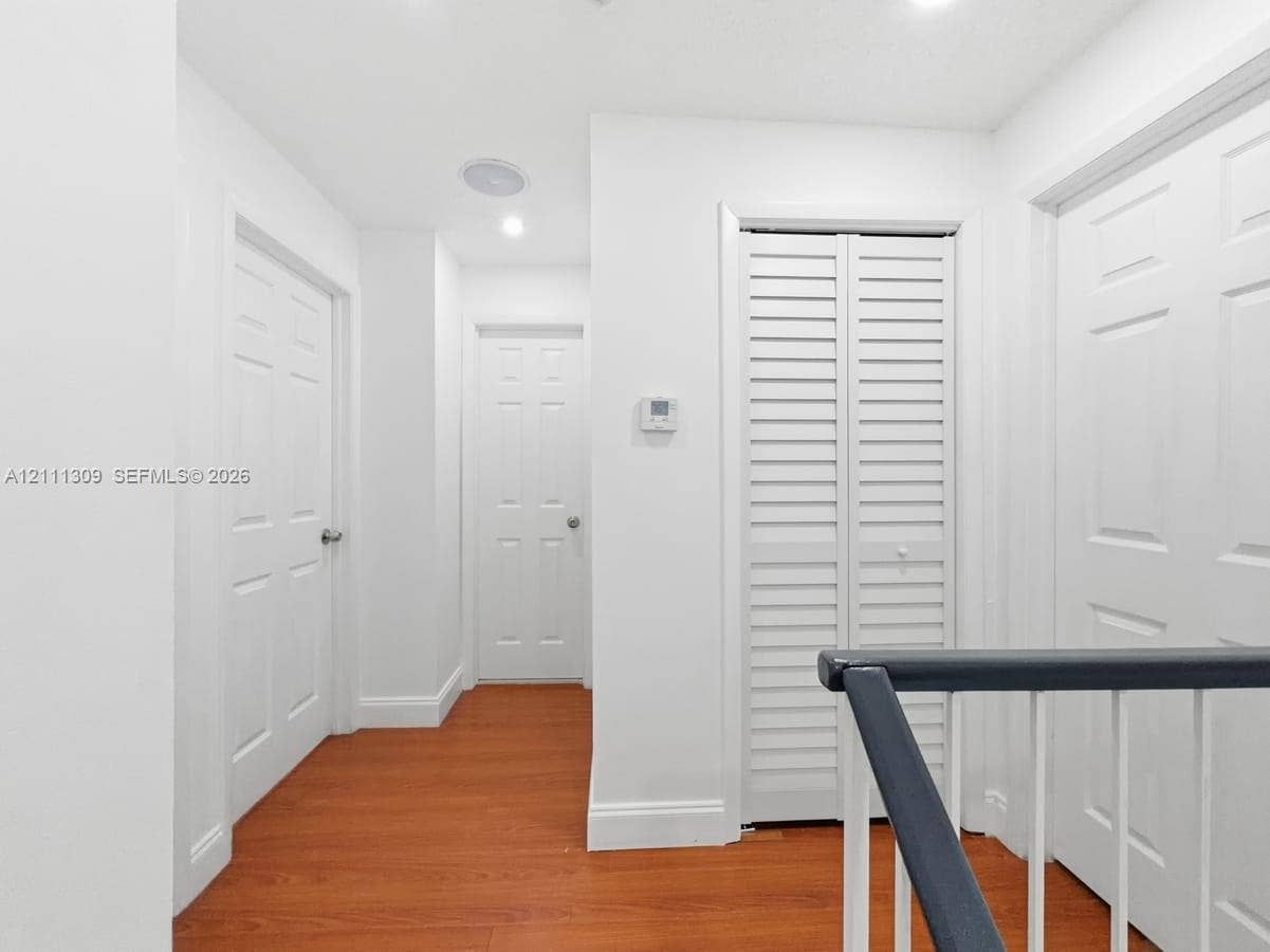 6518 Kendale Lakes Drive, #809, Miami, Miami, FL 33183 Hallway featuring wood-finish flooring, six-panel interior doors, louvered closet doors, and a contrasting handrail with vertical balusters