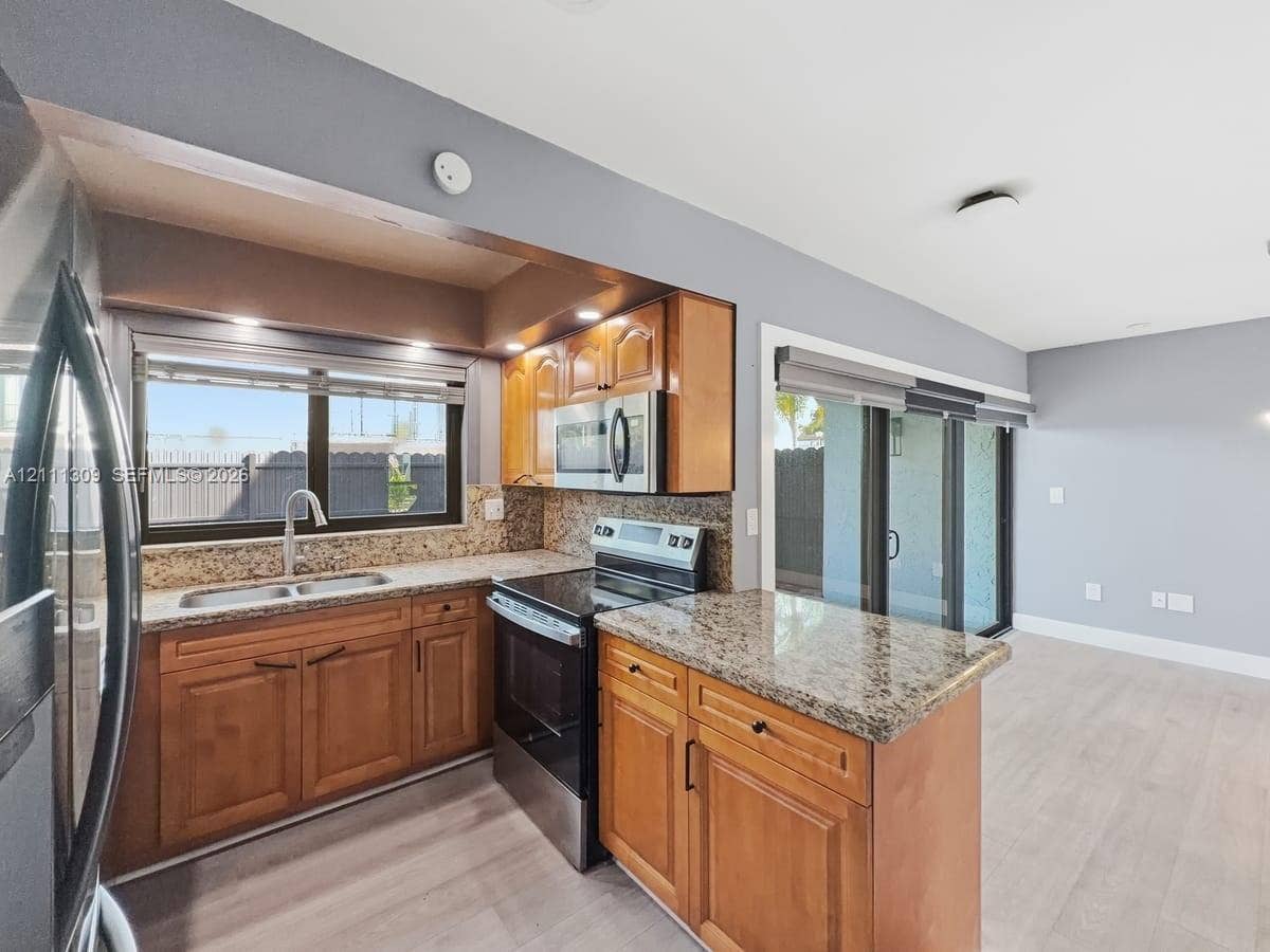6518 Kendale Lakes Drive, #809, Miami, Miami, FL 33183 Kitchen featuring wood cabinetry, stone-finish countertops, stainless steel appliances, wood-finish flooring, and sliding glass doors