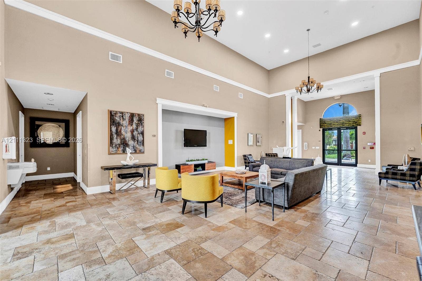 Expansive interior featuring high ceilings, stone-tile flooring, dual chandeliers, and an arched transom window