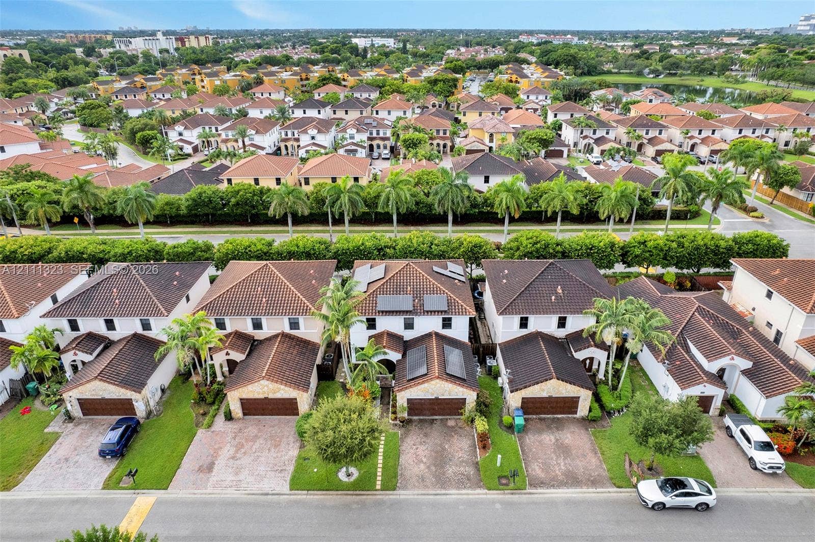 Aerial perspective of a multi-unit residential community featuring barrel-tile roofing, stone facade accents, paver driveways, and integrated solar panel systems