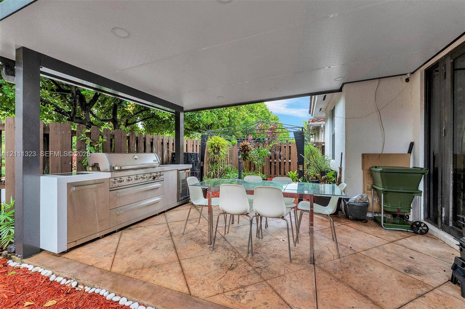 Covered outdoor patio featuring stamped concrete flooring, a built-in stainless steel kitchen module, recessed ceiling lighting, and a fenced perimeter