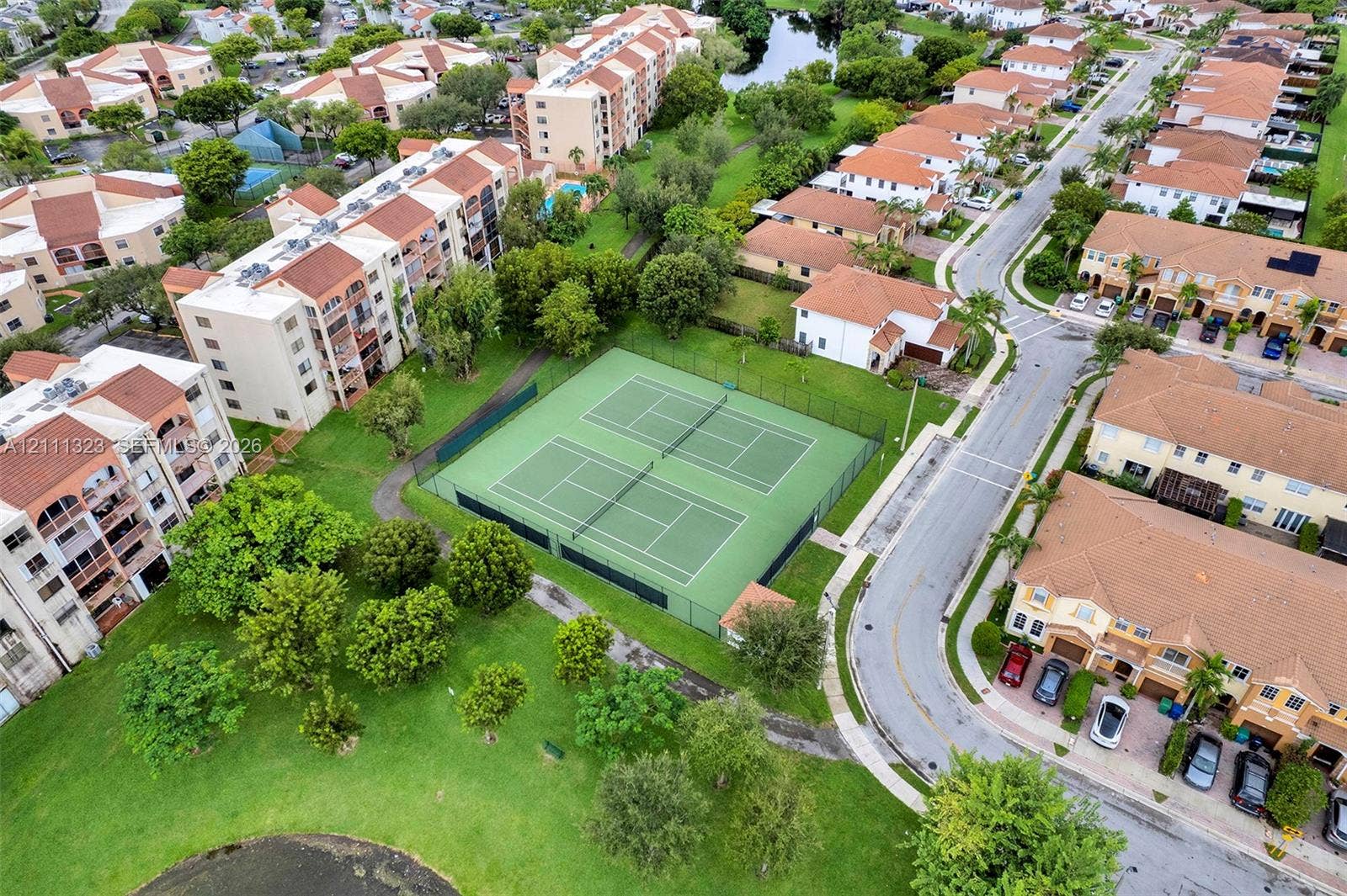 Aerial perspective of dual tennis courts featuring chain-link fencing, manicured green space, and mature trees