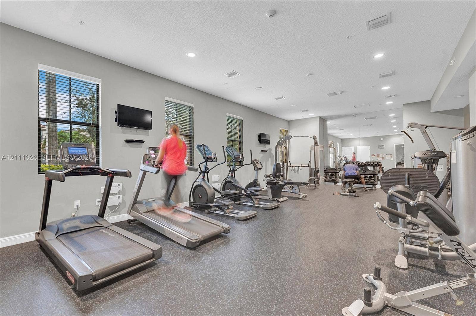 Fitness center featuring rubber flooring, recessed ceiling lighting, and multiple windows with horizontal blinds