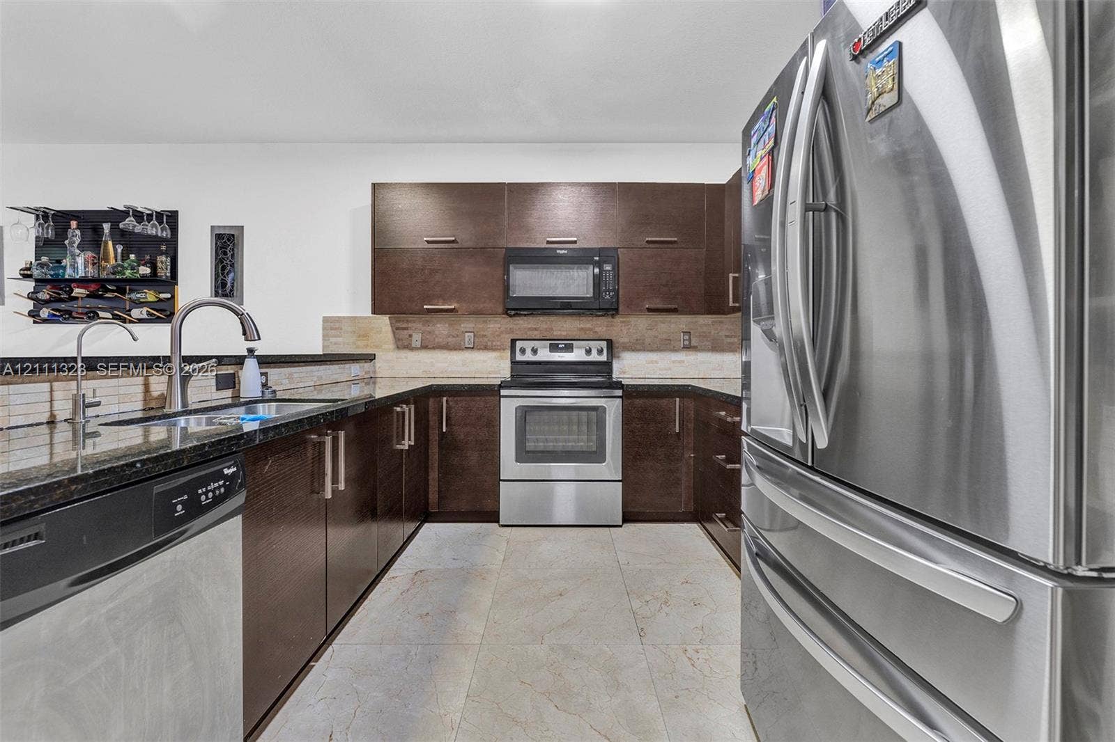 Kitchen featuring dark wood-finish cabinetry, stainless steel appliances, a stone countertop, a tile backsplash, and light-toned tile flooring