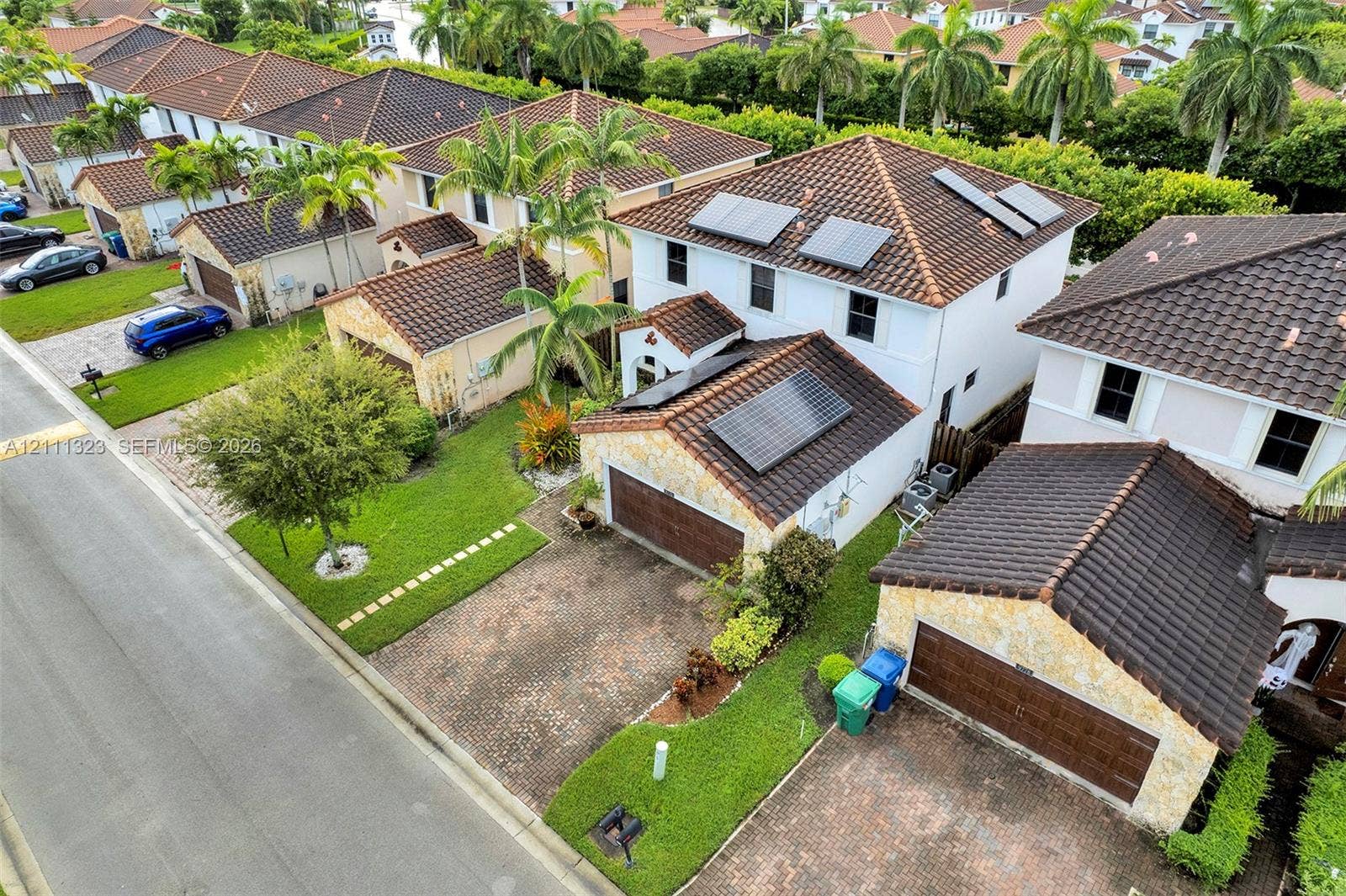 Two-story residence featuring a tile roof, solar panel array, stone-veneer exterior accents, paved driveway, and attached garage