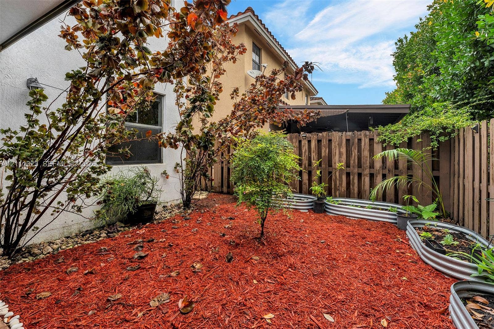 Private outdoor space featuring ground-level garden beds with corrugated metal framing, perimeter wood fencing, and mulch landscaping