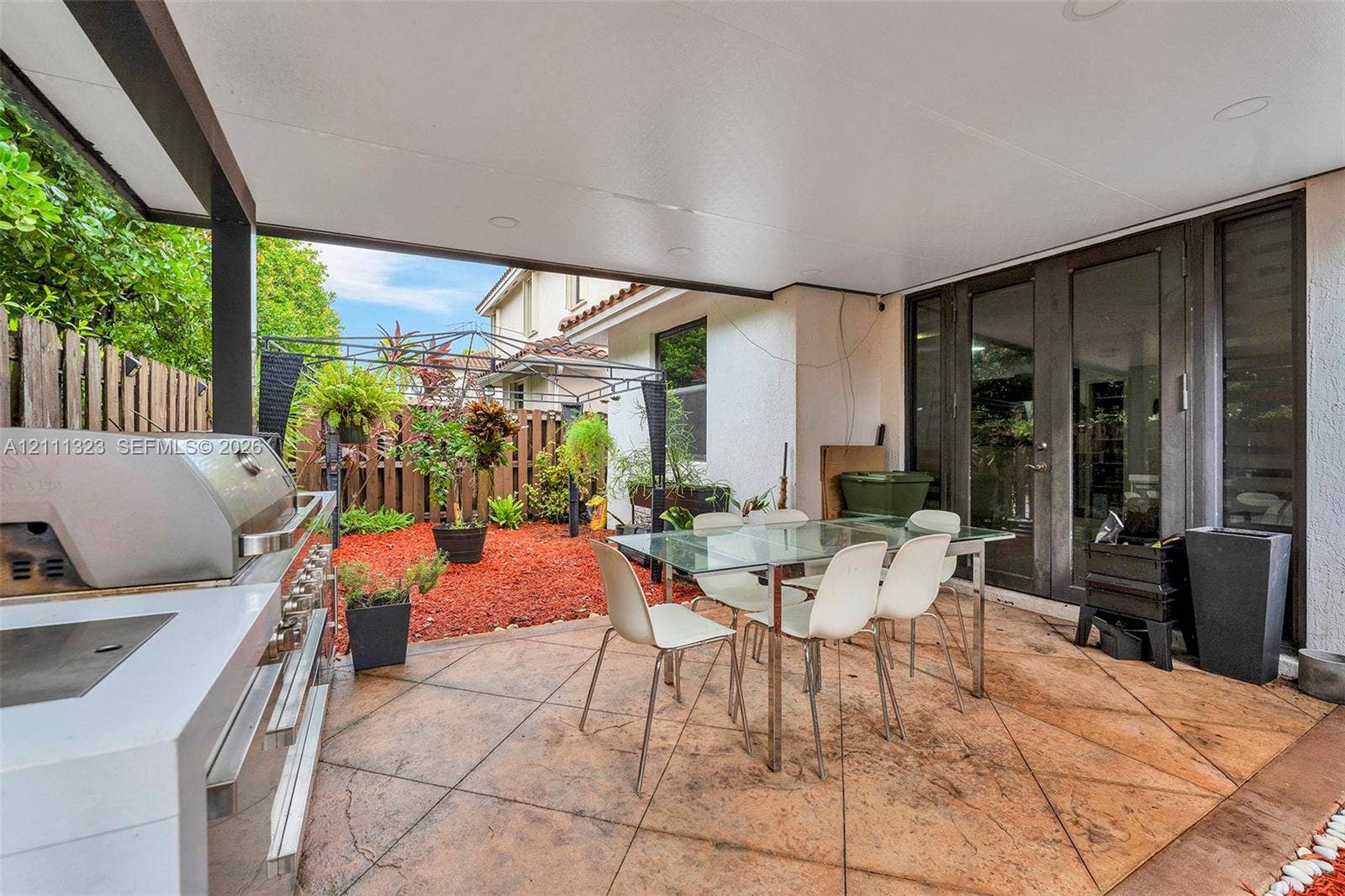 Covered patio featuring stamped concrete flooring, a built-in outdoor kitchen with a stainless steel grill, recessed lighting, and glass panel doors