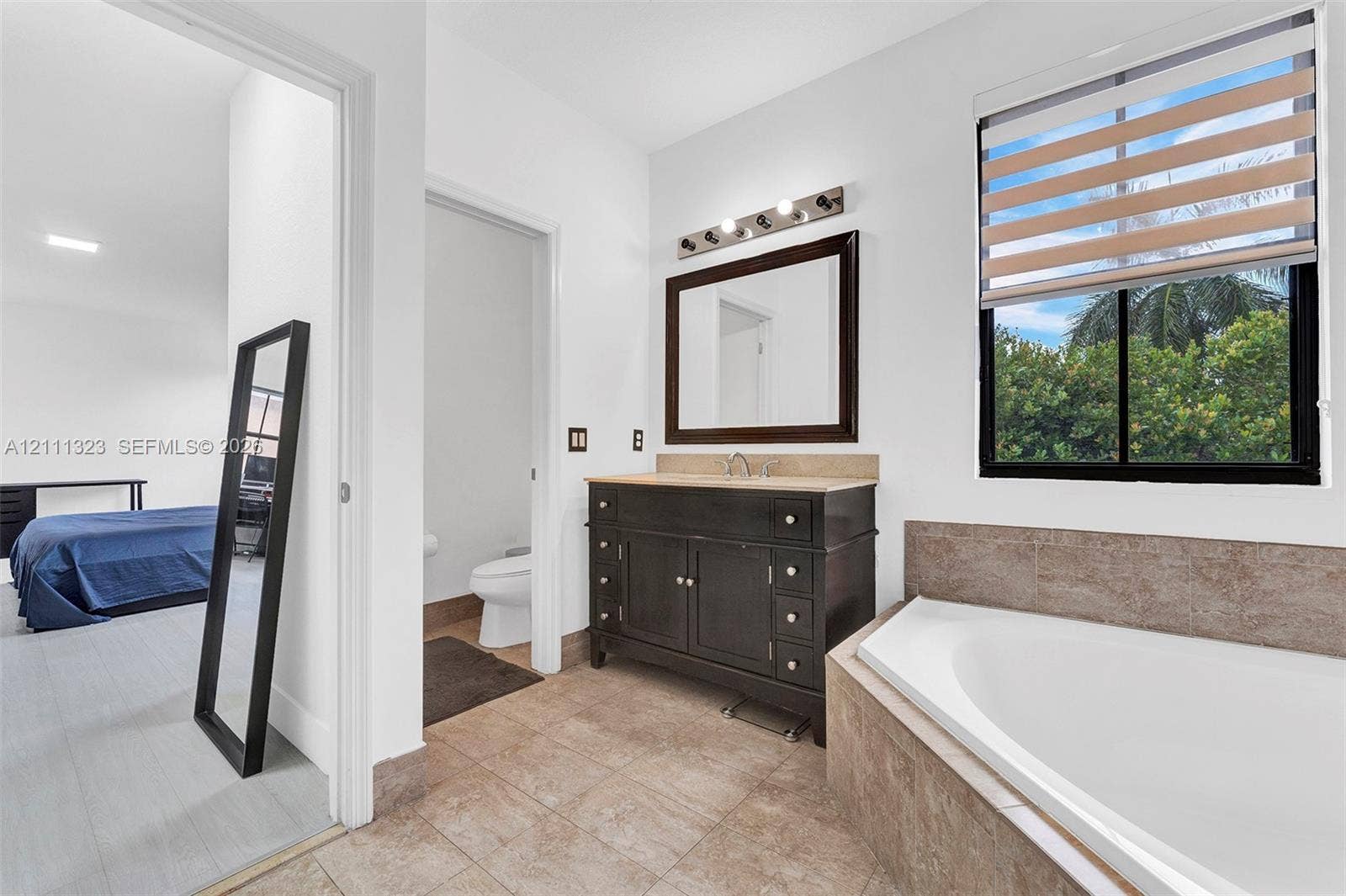 Bathroom featuring a vanity with dark cabinetry, stone-surfaced countertop, built-in soaking tub, multi-light fixture, and ceramic tile flooring