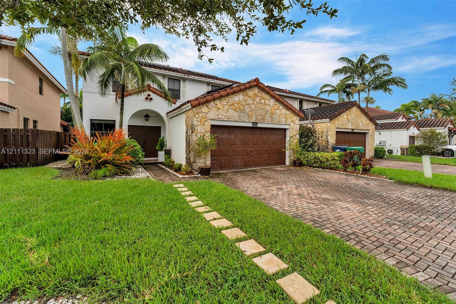 Two-story residence featuring a stone-clad facade, red tile roofing, multi-car garage, and a brick-paver driveway