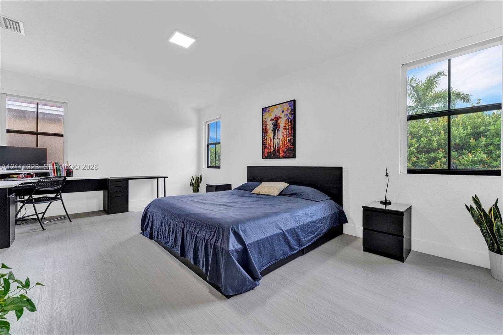 Spacious room featuring neutral walls, light wood-finish flooring, recessed lighting, and multiple windows with black trim