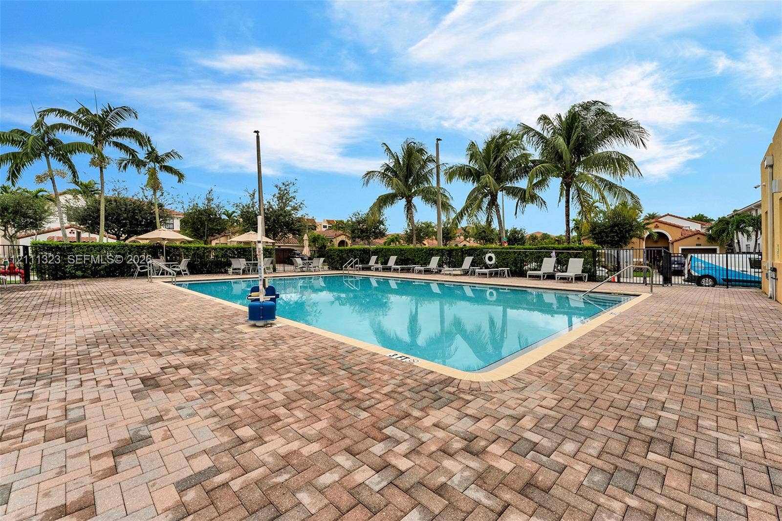 Outdoor swimming pool featuring a brick paver deck, perimeter landscaping, and metal pool fencing