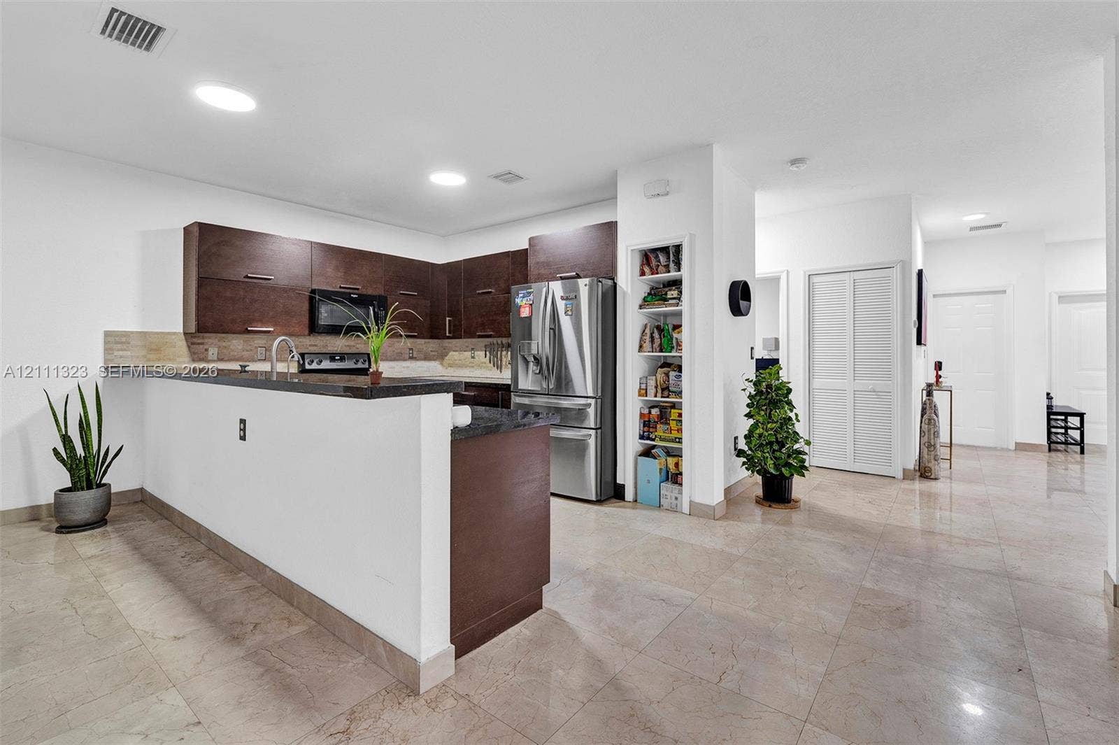 Kitchen featuring dark wood-finish cabinetry, stone countertops, stainless steel appliances, a built-in pantry, and large-format tile flooring