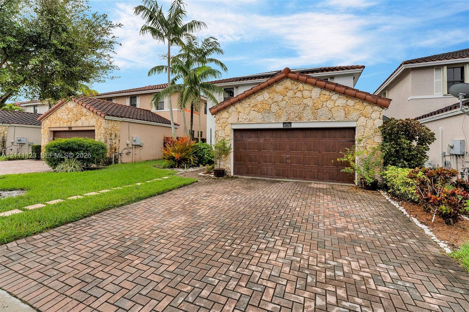 Two-story exterior featuring a stone-clad faade, brown tile roofing, a herringbone-patterned brick paver driveway, and an attached multi-car garage