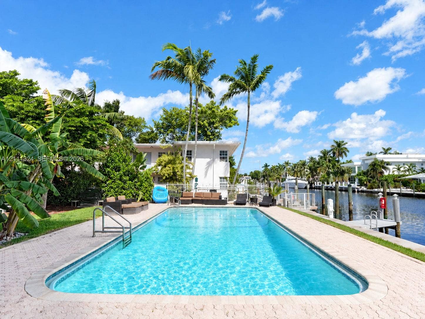 Rectangular in-ground swimming pool with integrated metal handrails, paver stone pool deck, and direct water frontage featuring a private dock