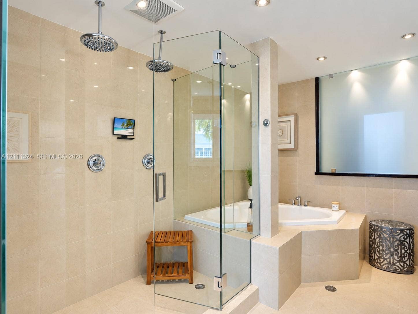 Walk-in glass shower featuring dual rainfall showerheads and built-in screen, accompanied by a corner soaking tub with integrated tiled surround