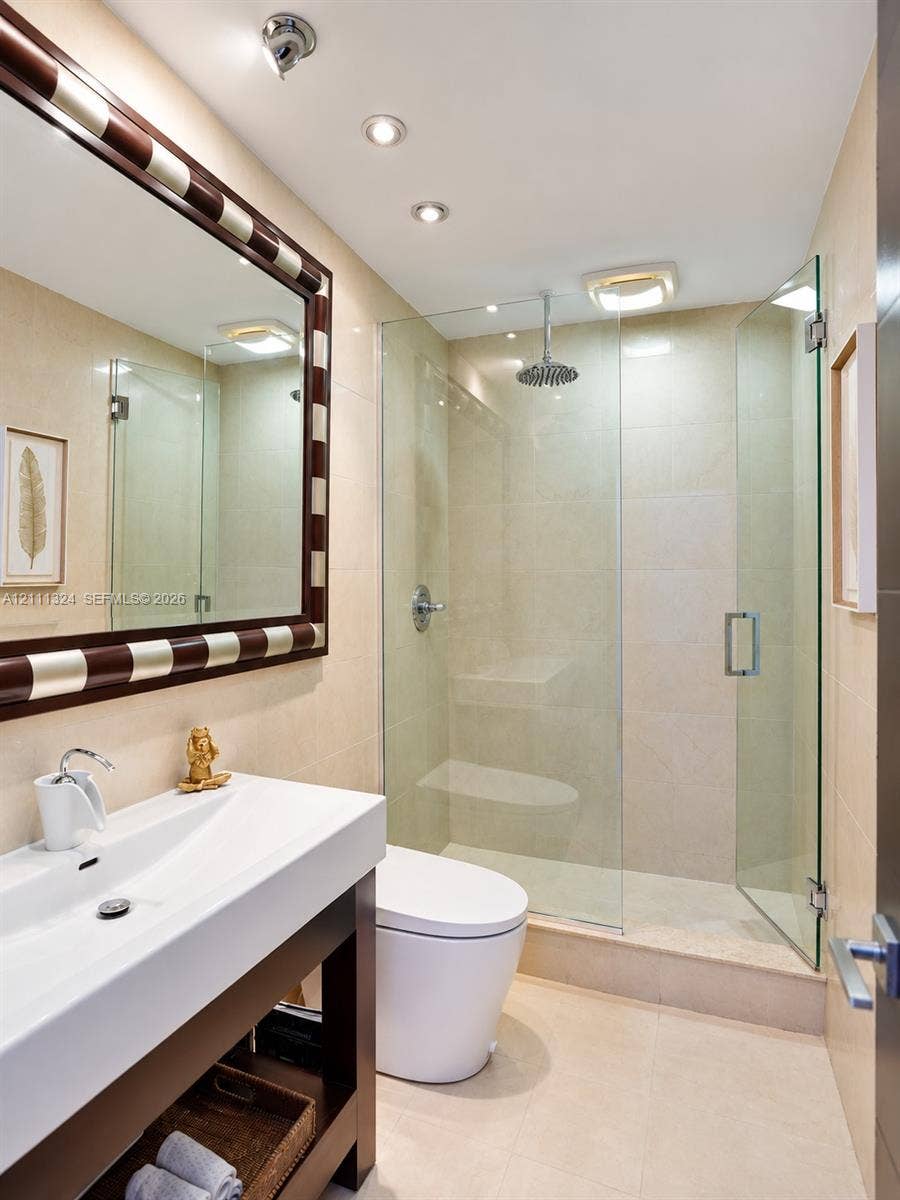 Bathroom featuring a floating vanity with a rectangular sink, walk-in shower with a glass enclosure and rain-style showerhead, recessed lighting, and large-format tile wall cladding