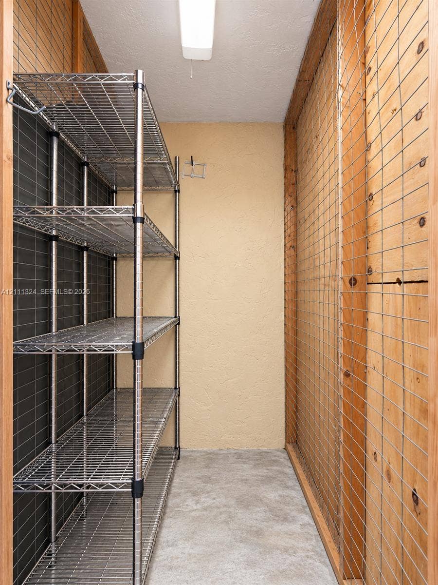 Storage space featuring metal wire shelving, plywood-paneled walls with wire grid overlays, and concrete flooring