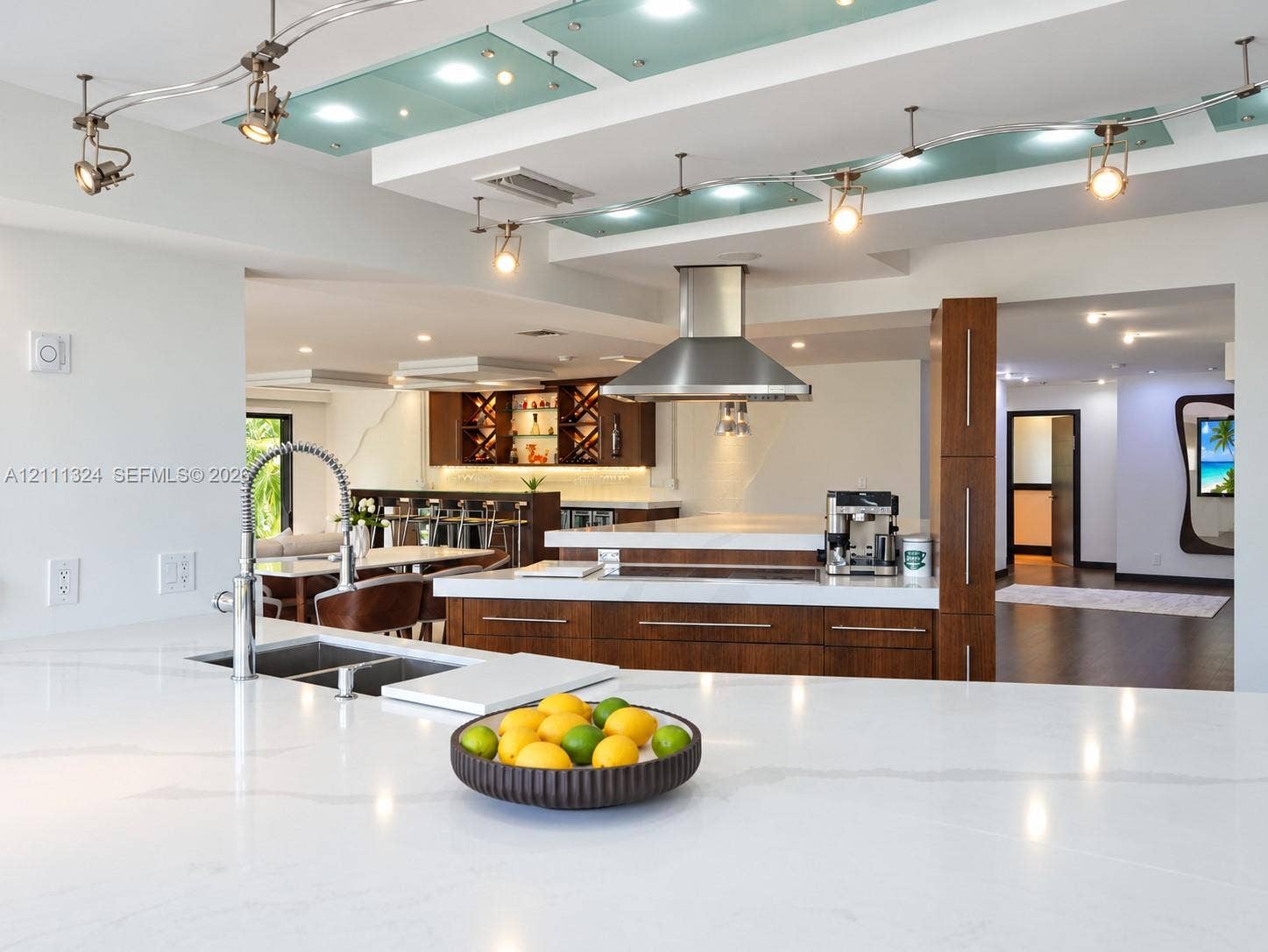 Custom kitchen featuring wood-finish cabinetry, white stone countertops, stainless steel range hood, glass-panel ceiling accents, and adjustable track lighting
