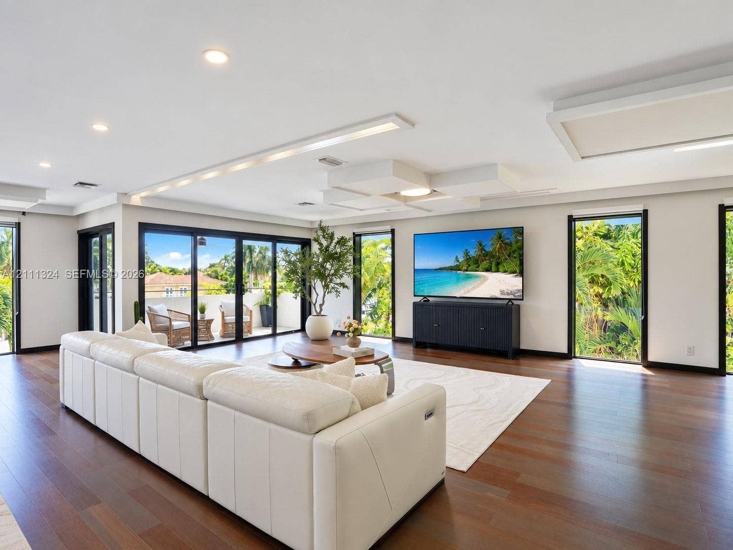 Open-concept interior featuring wood-finish flooring, recessed lighting, custom tiered ceiling architecture, and floor-to-ceiling glass sliding doors