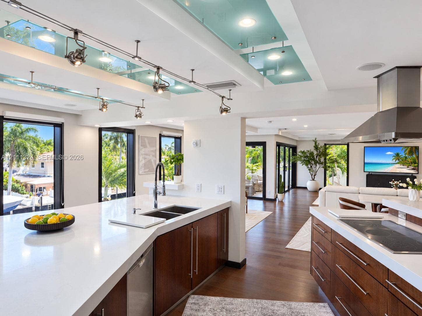 Kitchen featuring dark wood-finish cabinetry, solid-surface countertops, track lighting with glass accent panels, a stainless steel range hood, and wood-finish flooring