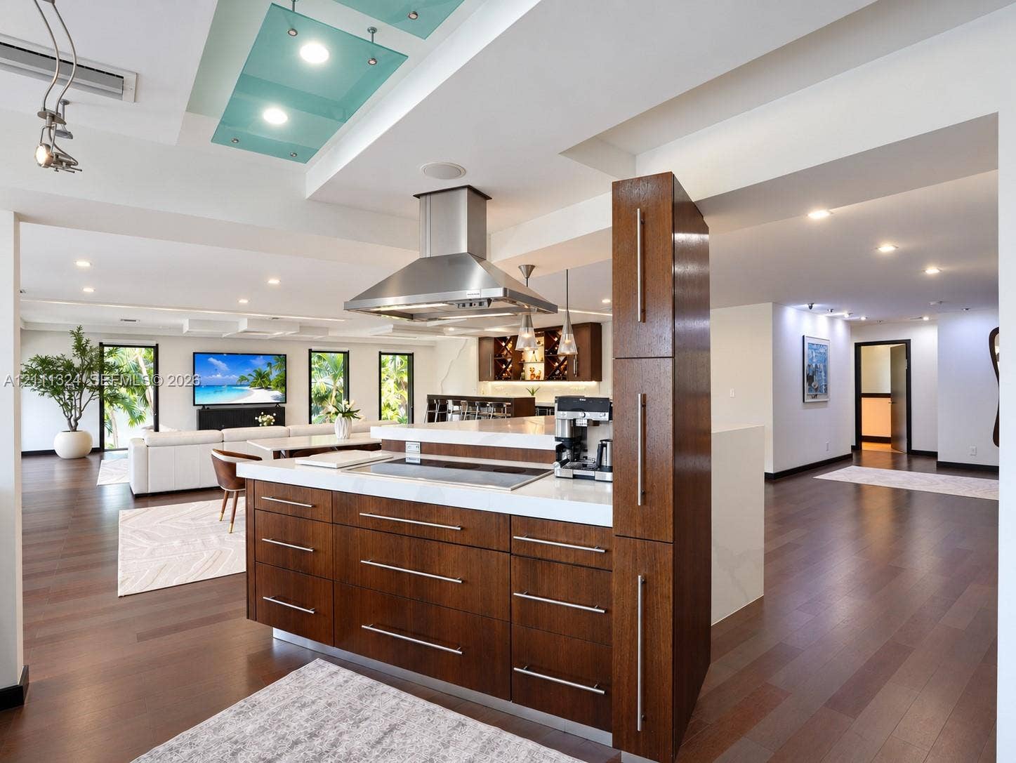 Kitchen island with dark wood-finish cabinetry, solid surface countertop, stainless steel cooktop, and stainless steel chimney range hood