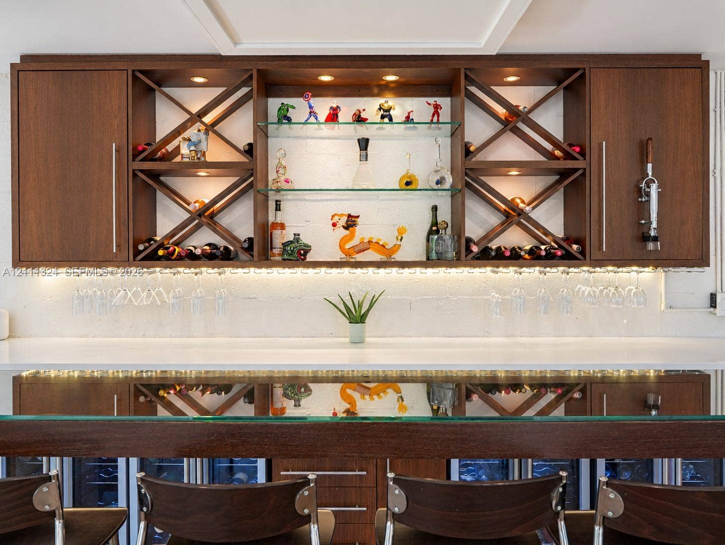 Custom built-in bar featuring wood cabinetry, integrated glass shelving, cross-hatch wine storage, under-cabinet lighting, and a white countertop