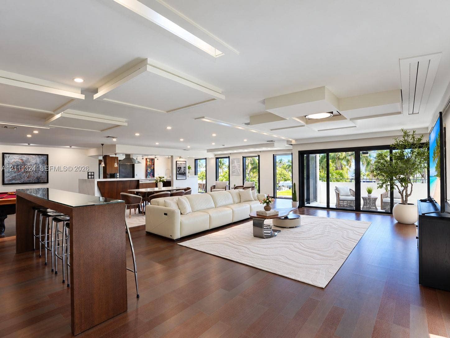 Open-concept interior featuring wood-finish flooring, custom geometric drop-ceiling detailing, recessed lighting, and expansive multi-panel sliding glass doors