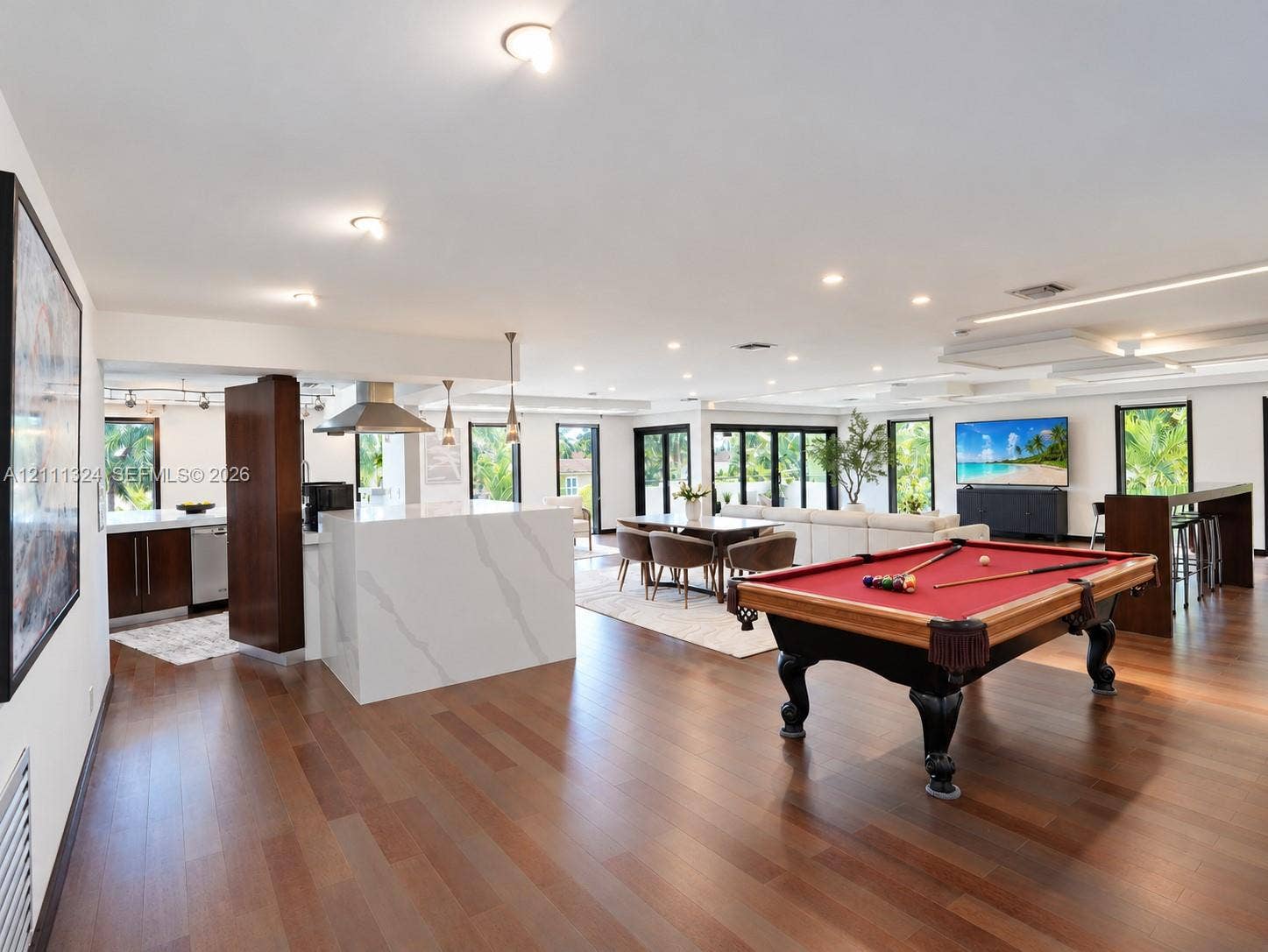 Open-concept interior featuring wood-finish flooring, recessed lighting, a stone-surfaced kitchen island, and multiple floor-to-ceiling glass panel doors
