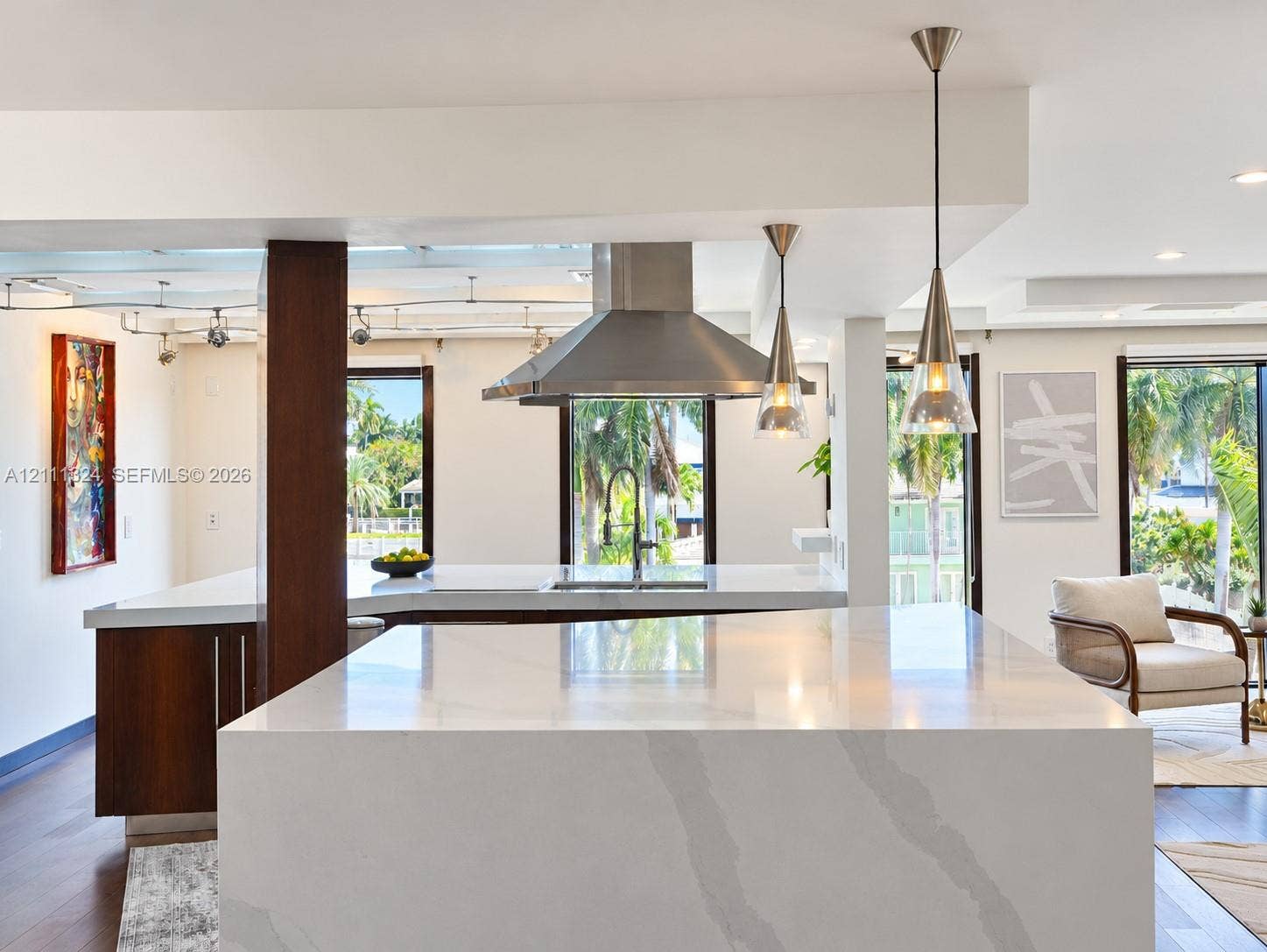 Kitchen featuring a waterfall-edge stone island, wood-finish cabinetry, stainless steel range hood, gooseneck faucet, and conical pendant lighting