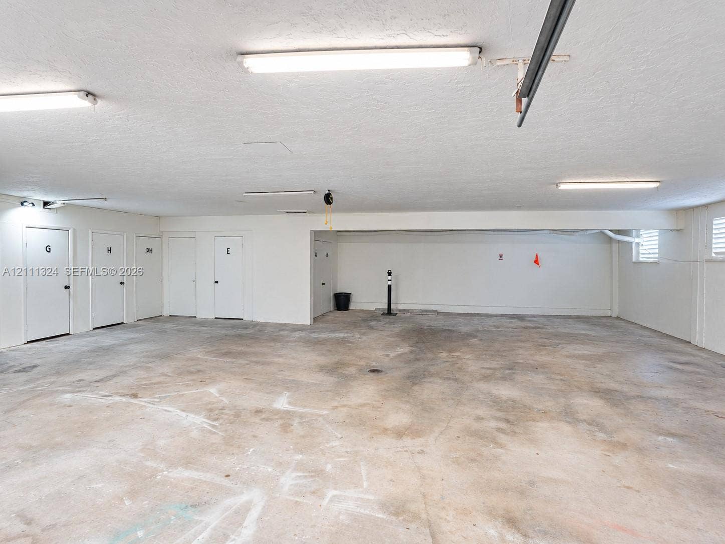 Expansive parking area featuring concrete flooring, multiple integrated storage units, and overhead fluorescent lighting
